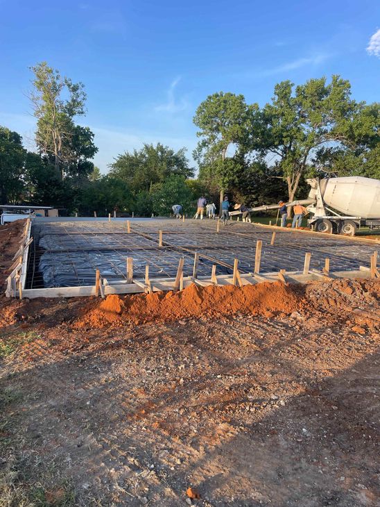 A concrete truck is pouring concrete into a dirt field.