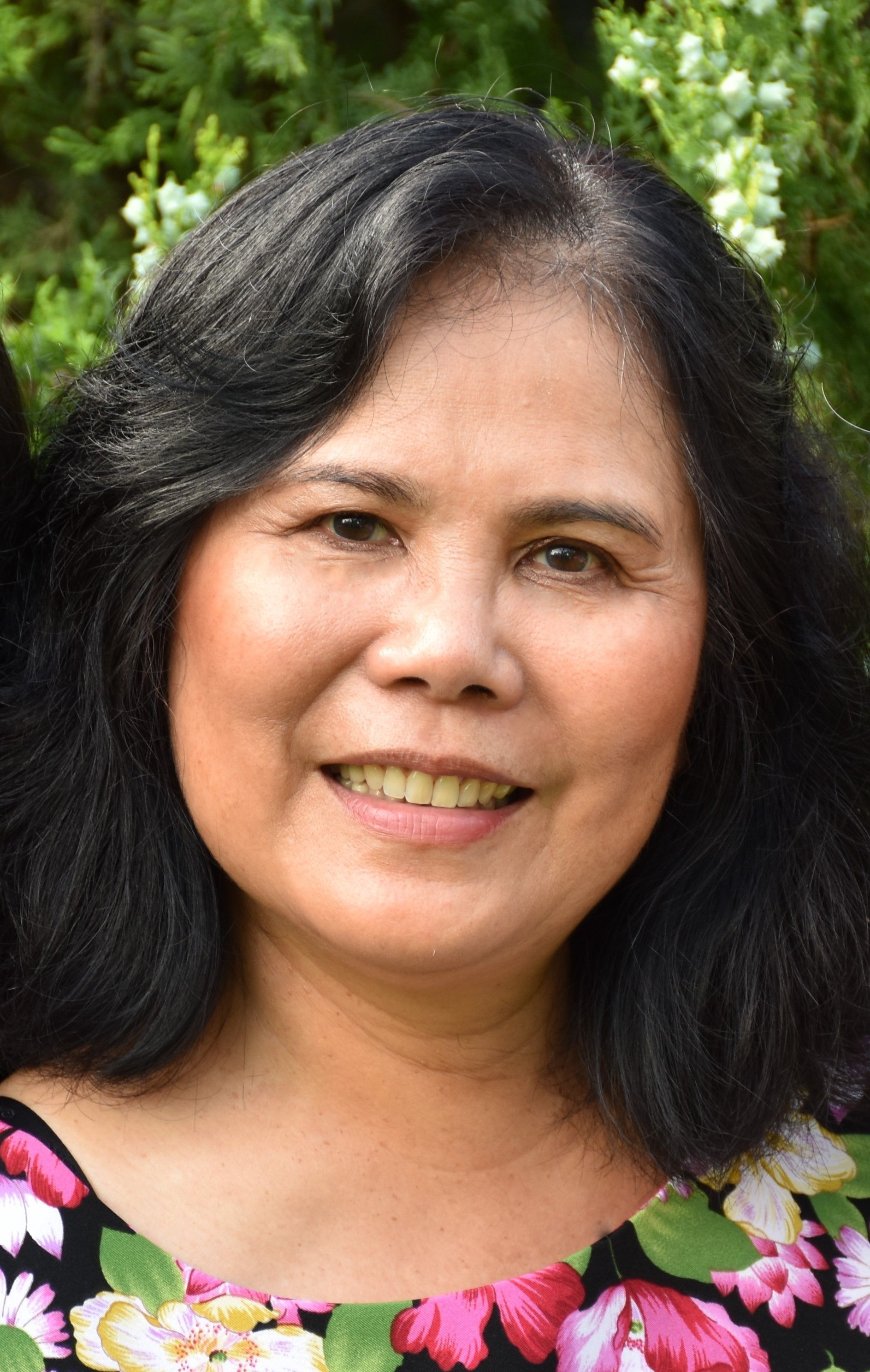 Woman with dark hair smiles; floral top, green background.