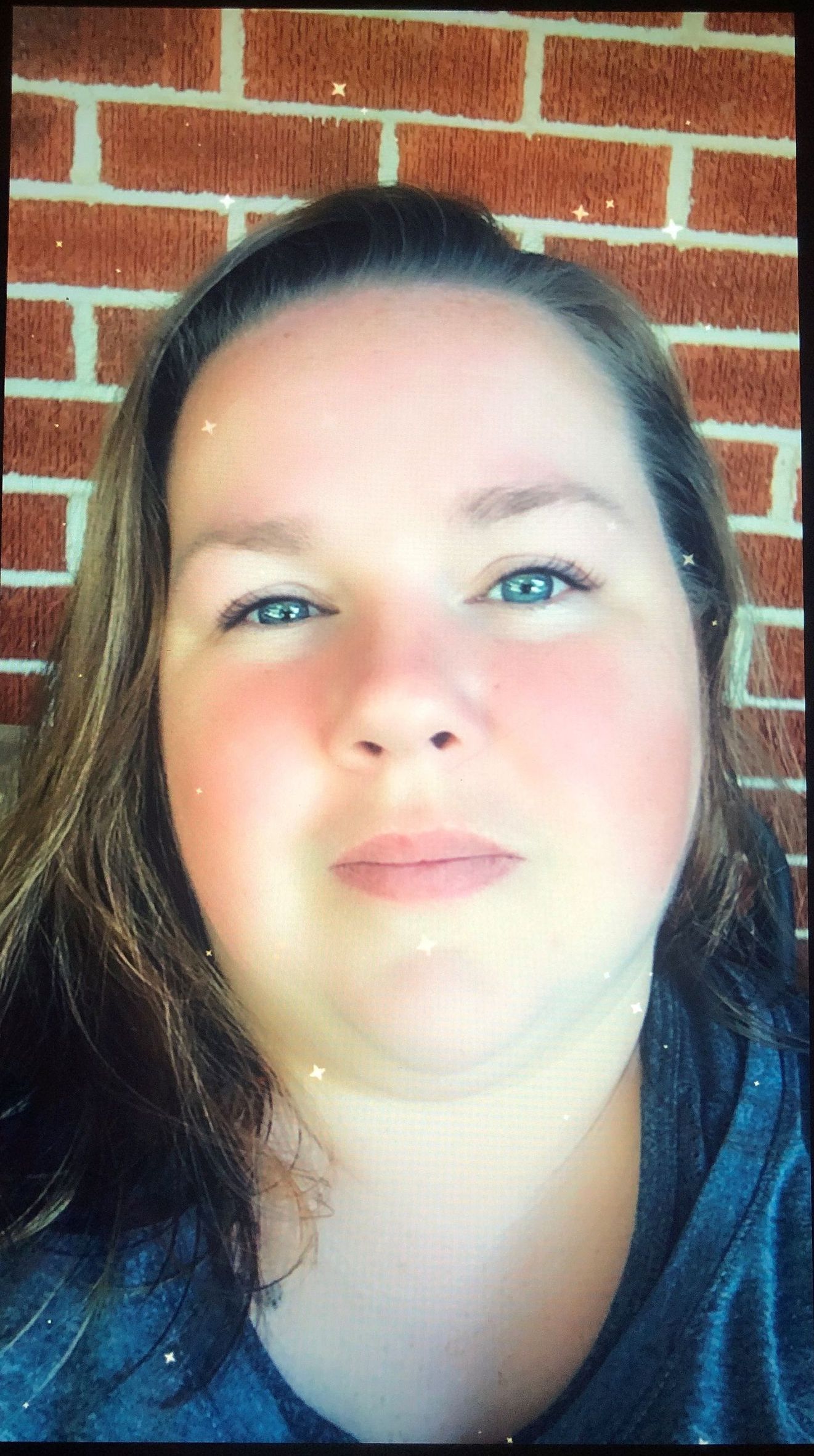 Woman with fair skin and blue eyes in front of a brick wall; she's wearing a blue shirt.