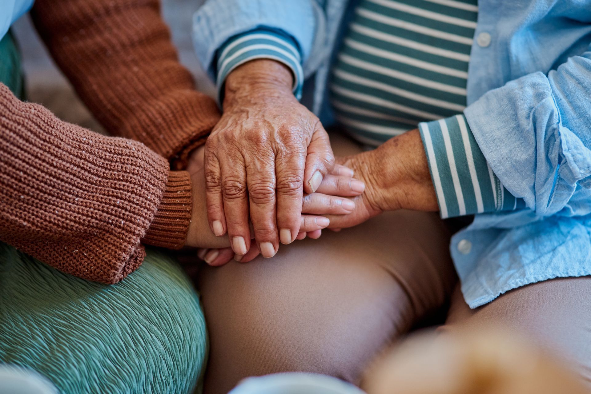 Two older women are sitting on a couch holding hands.