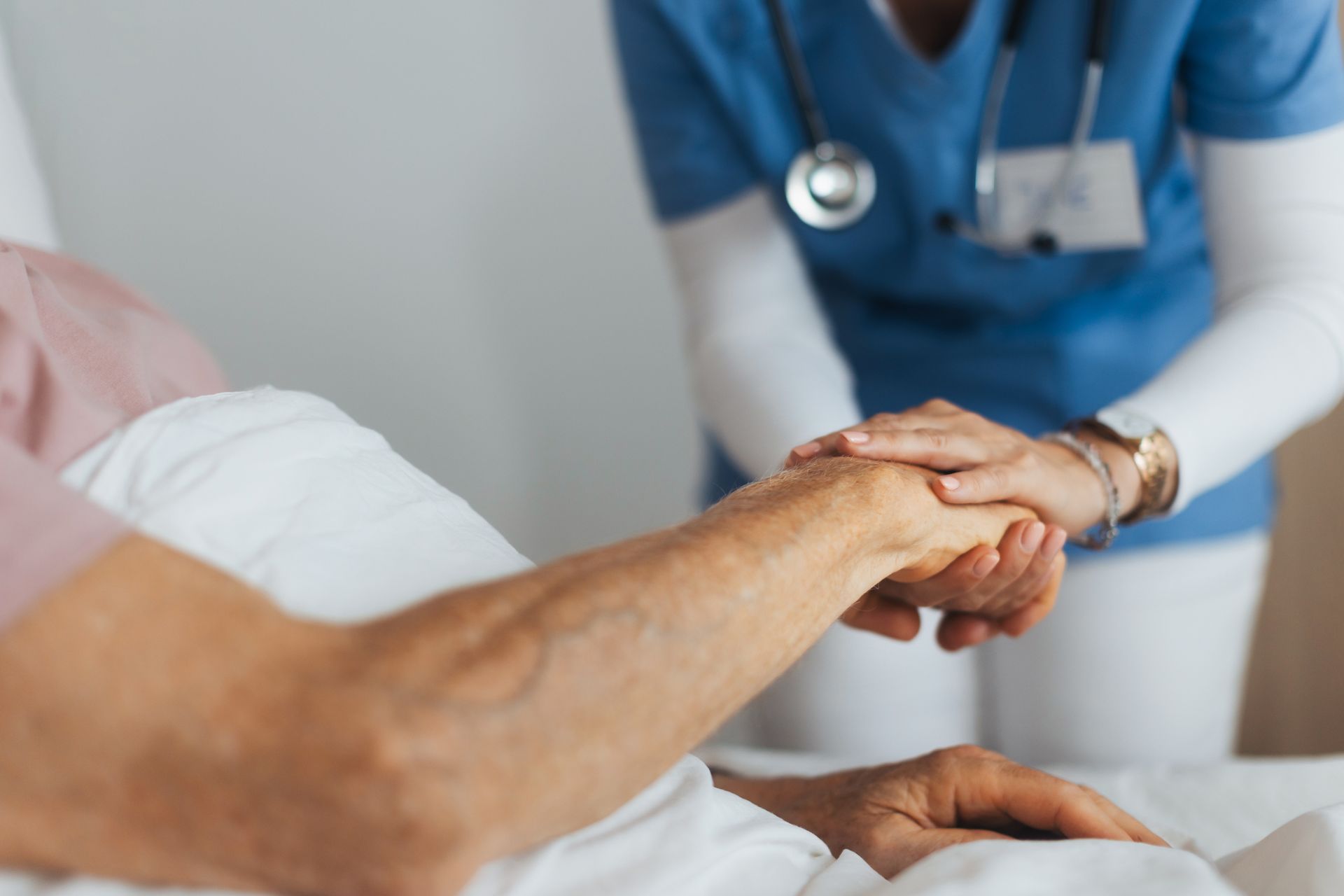 Nurse in blue scrubs holding patient's hand in hospital bed. Nurse in blue scrubs holding patient's hand in hospital bed.