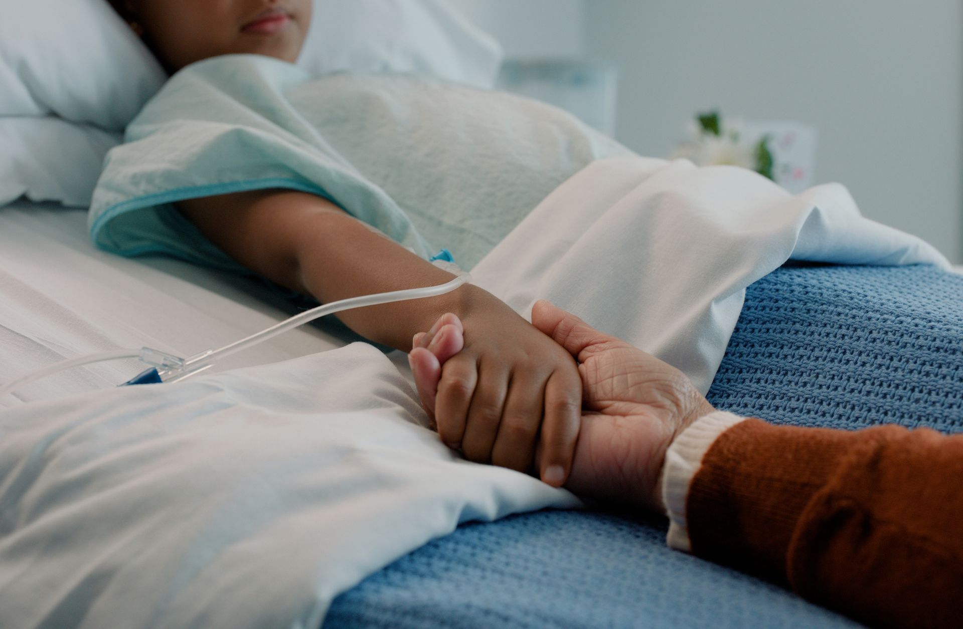 Caregiver holding the hand of a child in a hospital bed, showcasing gentle pediatric hospice care.