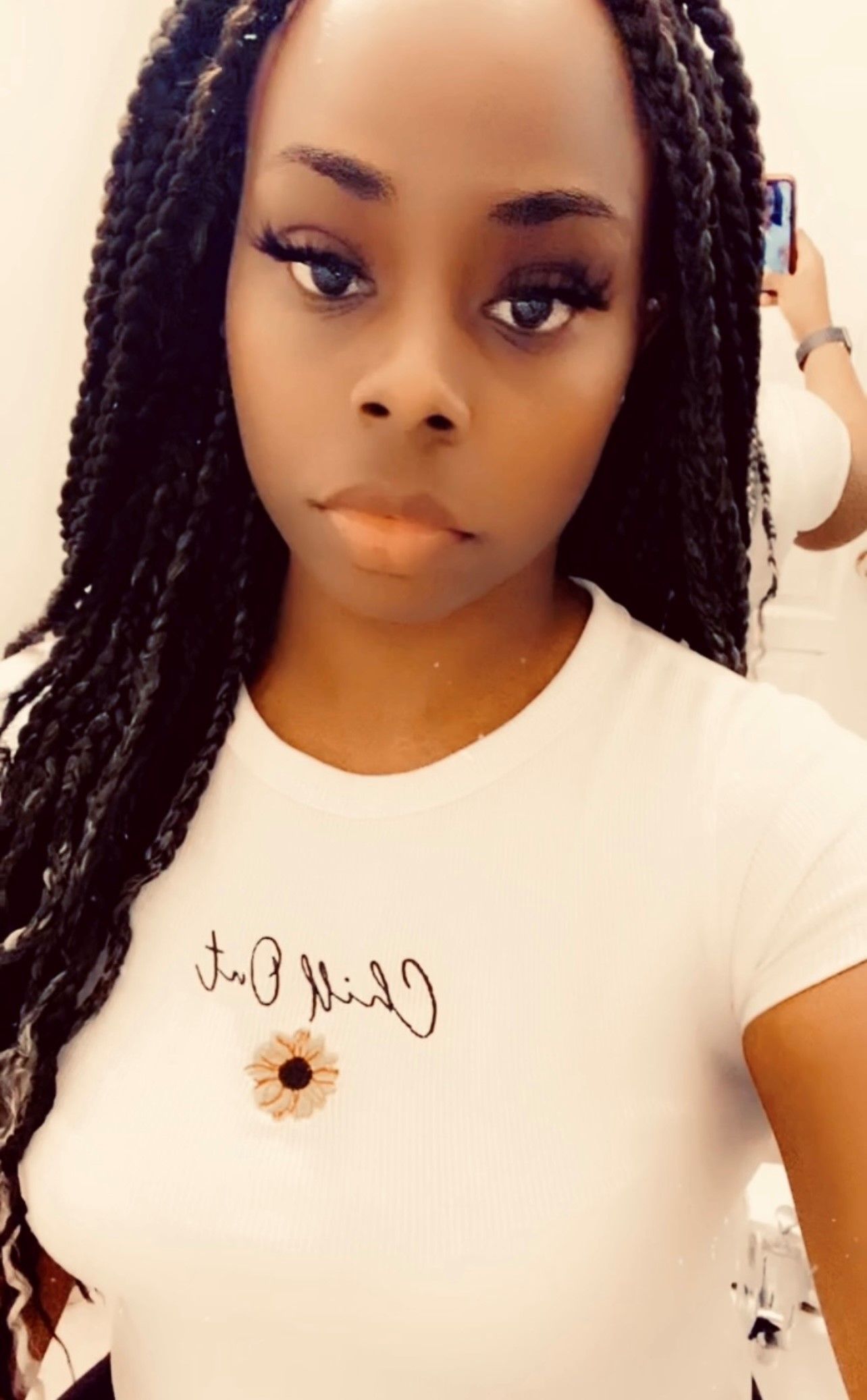 Woman with braided hair wearing a white t-shirt, taking a selfie indoors.