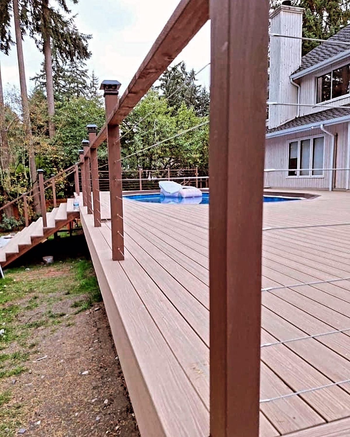 Wooden deck with railing, stairs, and a pool. House in the background.