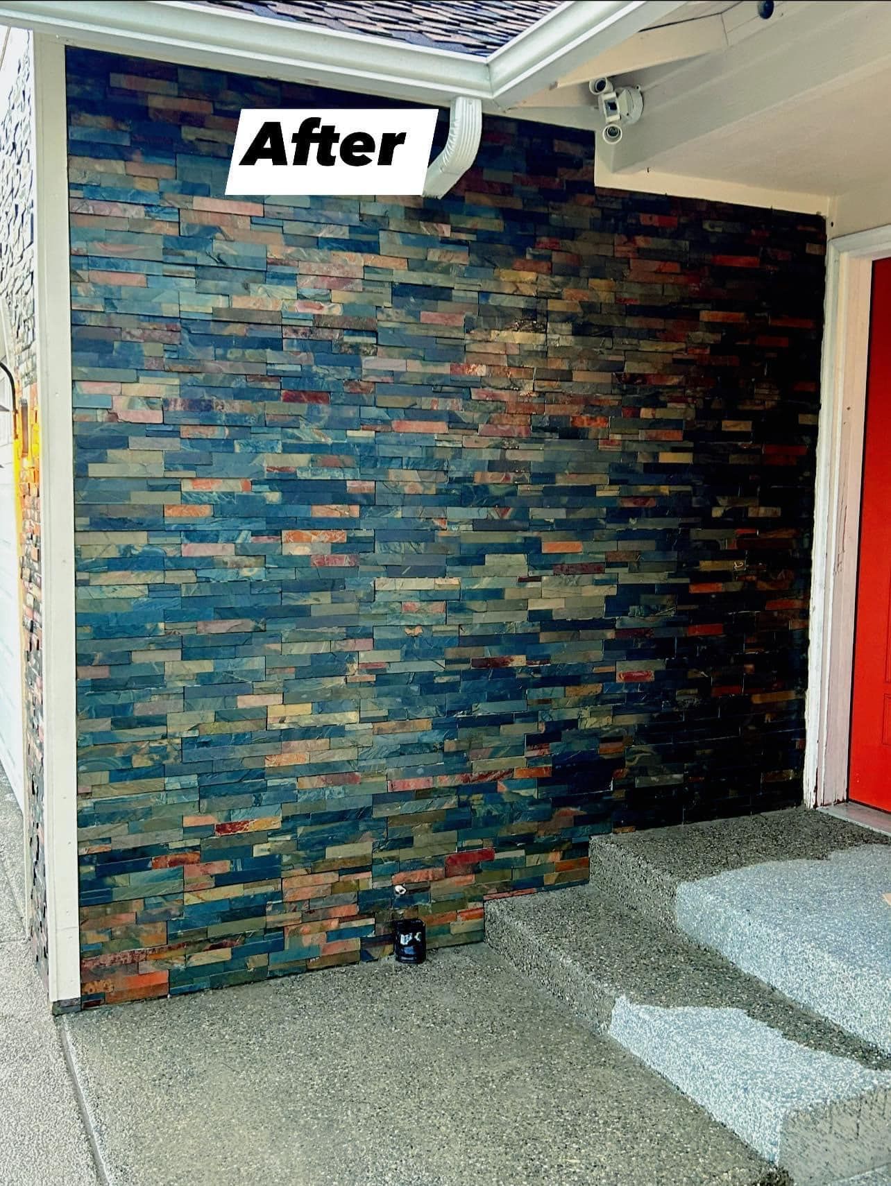 Exterior wall with dark, textured stone veneer; concrete porch, red door.