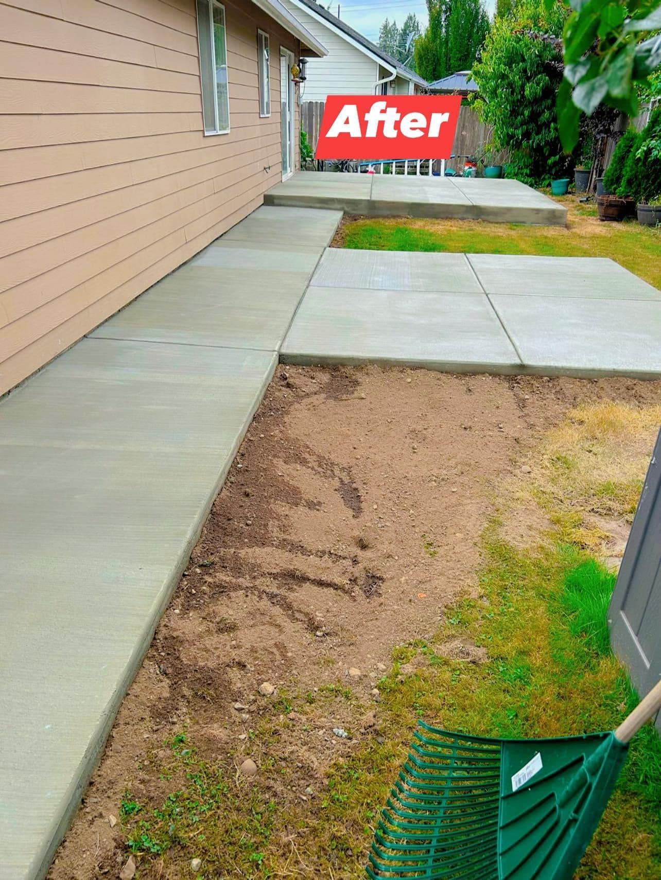 Freshly poured concrete walkway and patio next to a house, with raked dirt bed, green yard, and red