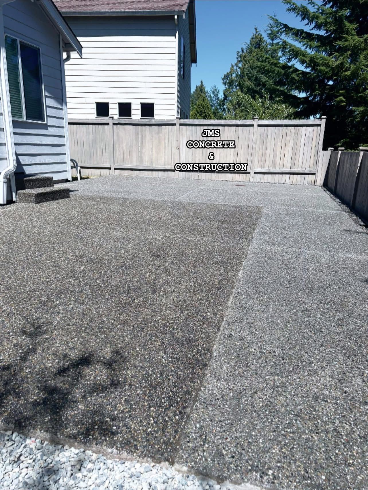 Gravel driveway next to a light blue house. A wooden fence is in the background. Sunny day.