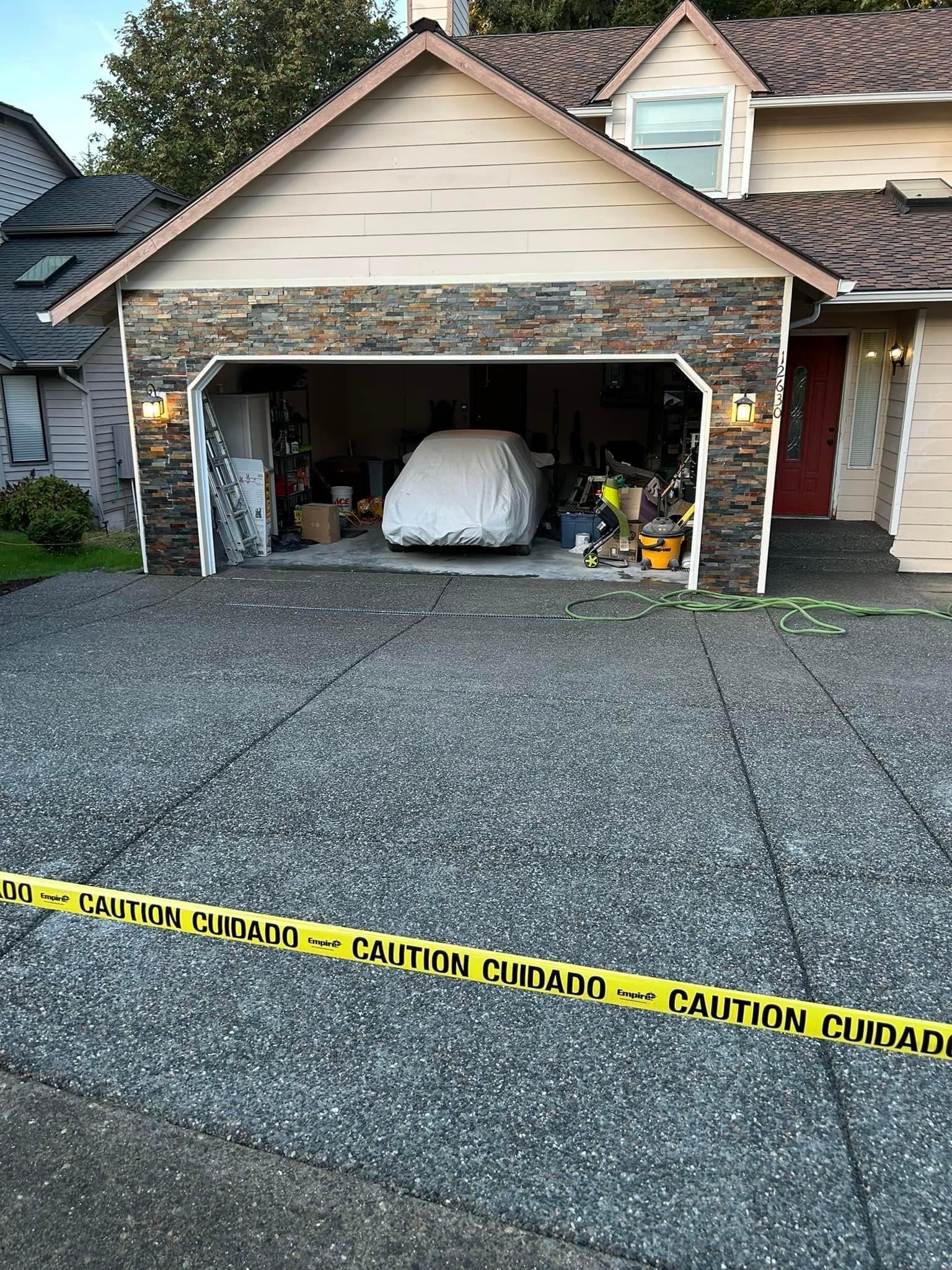 Garage of a house; car under a cover inside, caution tape across driveway.