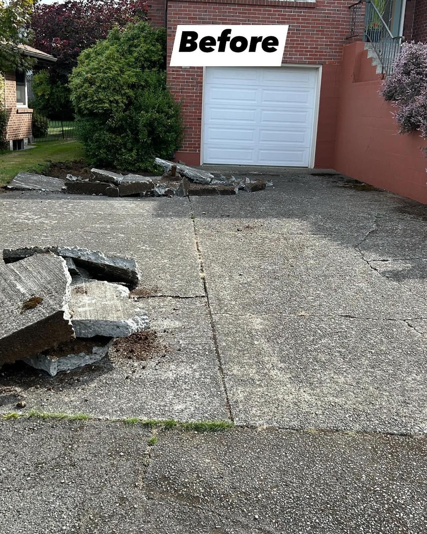 Cracked concrete driveway with chunks of broken concrete in front of a white garage door. 