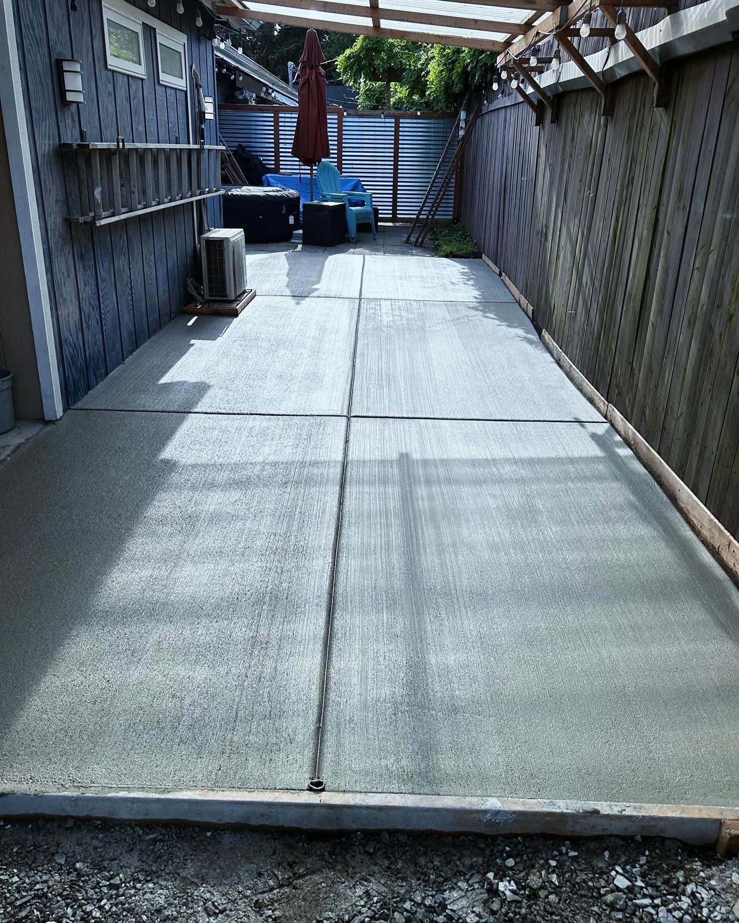 Concrete patio with a fence on either side. A ladder leans against the building.