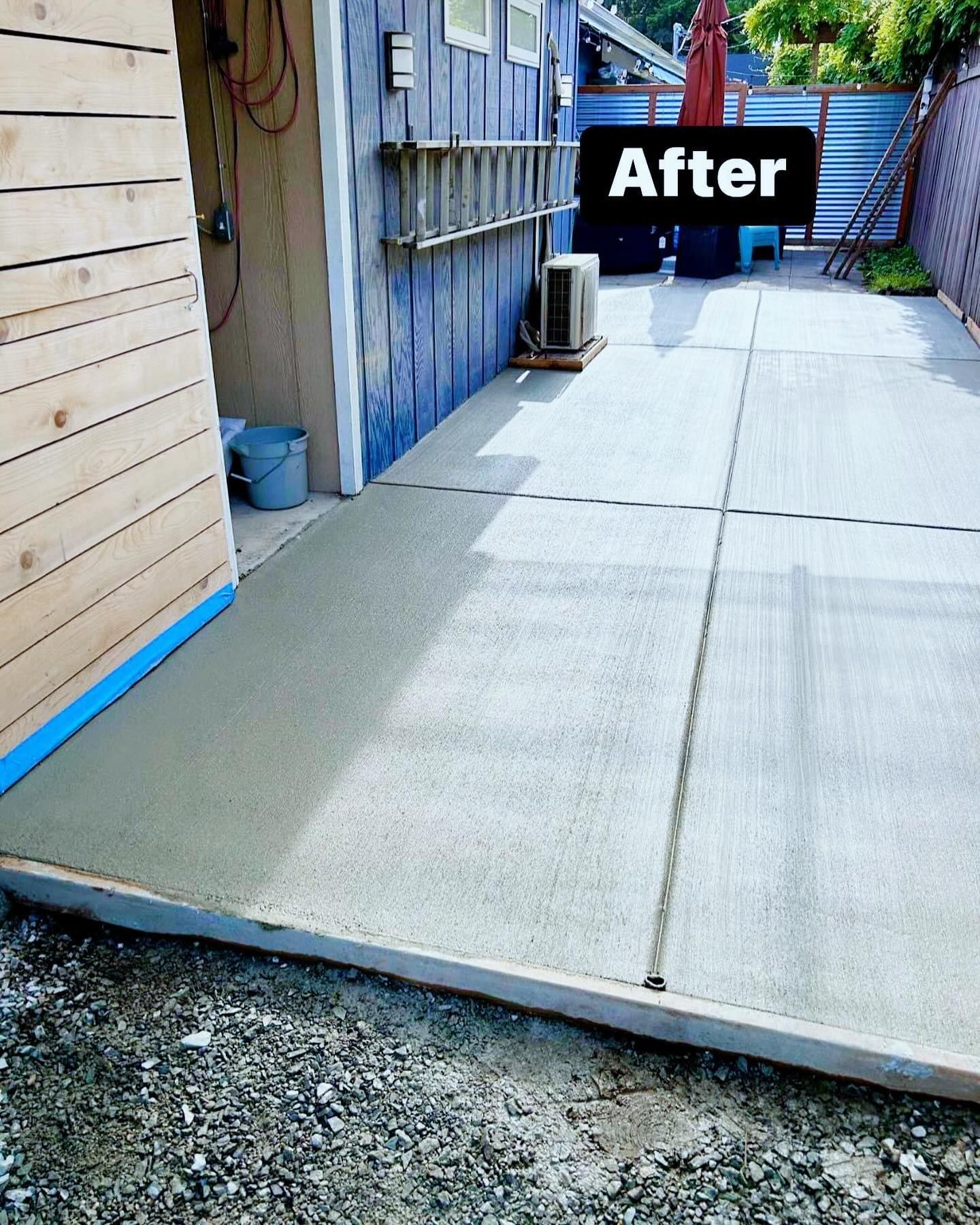 Freshly poured concrete patio; building with blue siding on the right, wooden structure on the left.