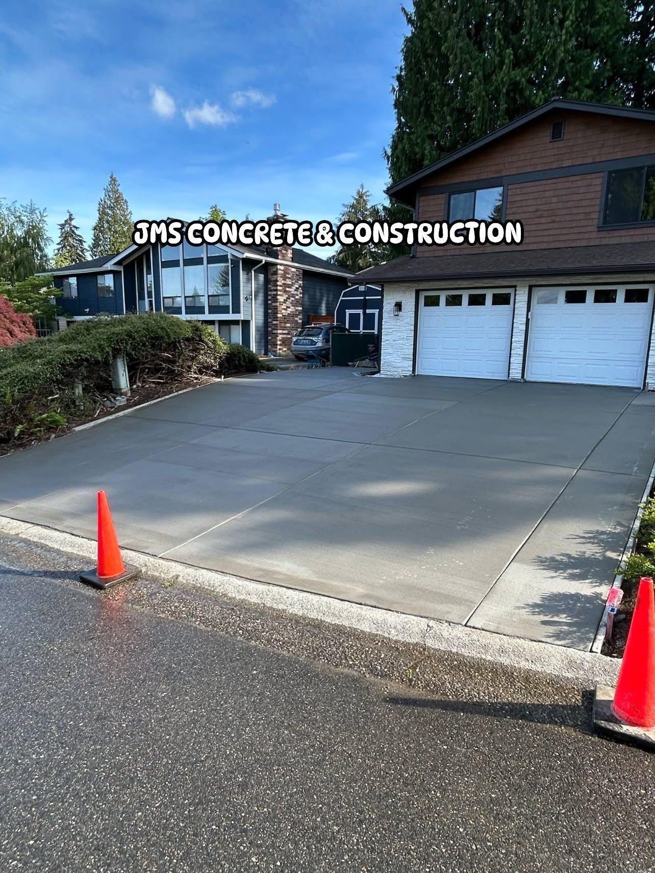 Freshly poured concrete driveway in front of a house, orange traffic cones on the edges.