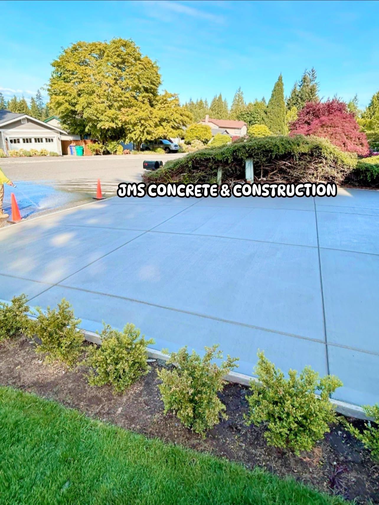 Newly poured concrete driveway with landscaping and a house in the background. Blue sky overhead.