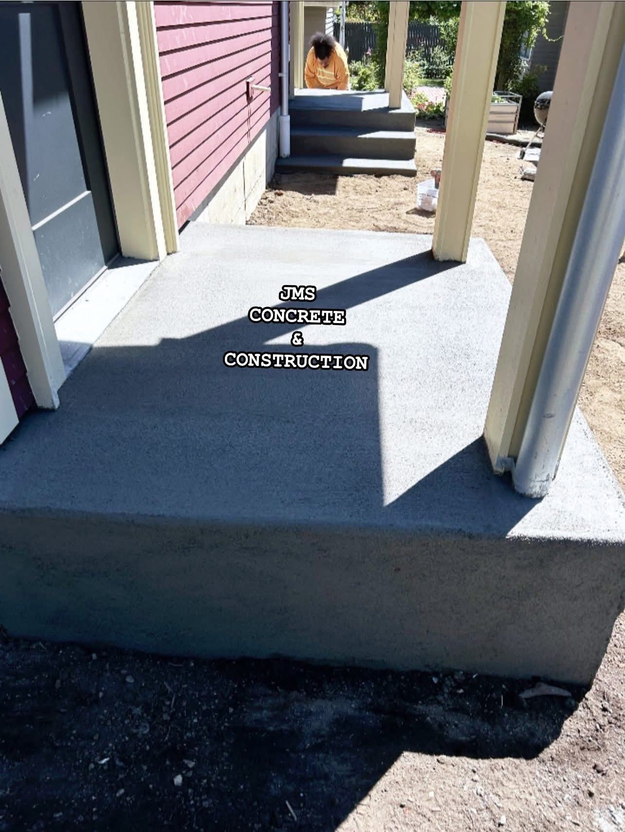 Concrete porch and steps next to a red-sided building, supported by white pillars.
