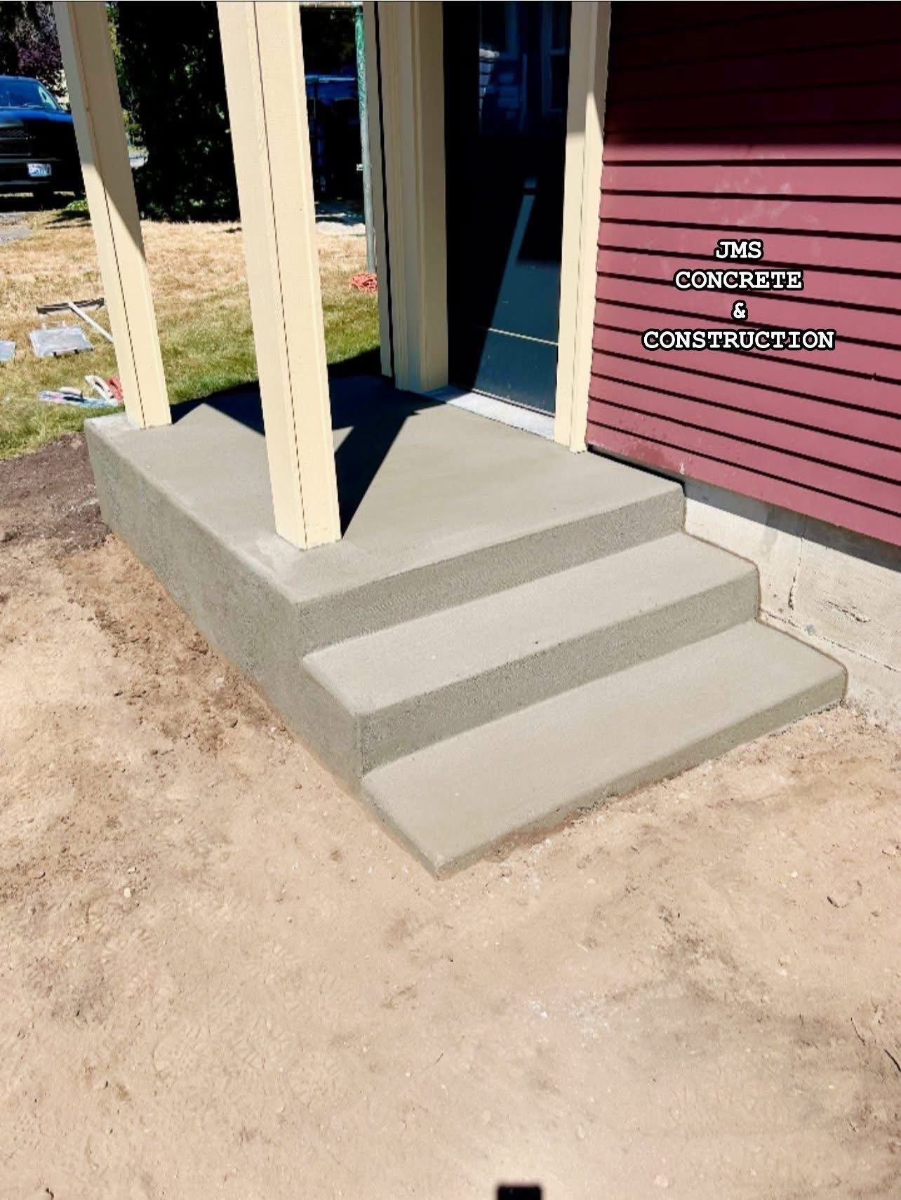 Gray concrete steps leading to a building's entrance. Wooden support columns and red siding are visible.