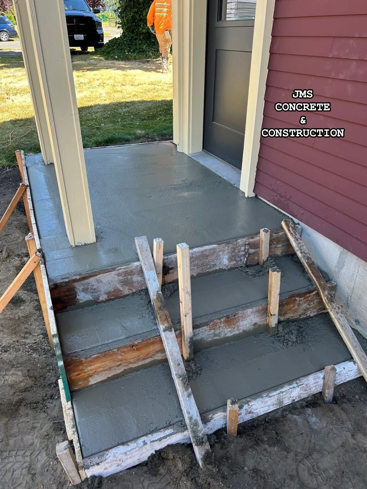 Freshly poured concrete steps and landing outside a building, with wood framing still in place.