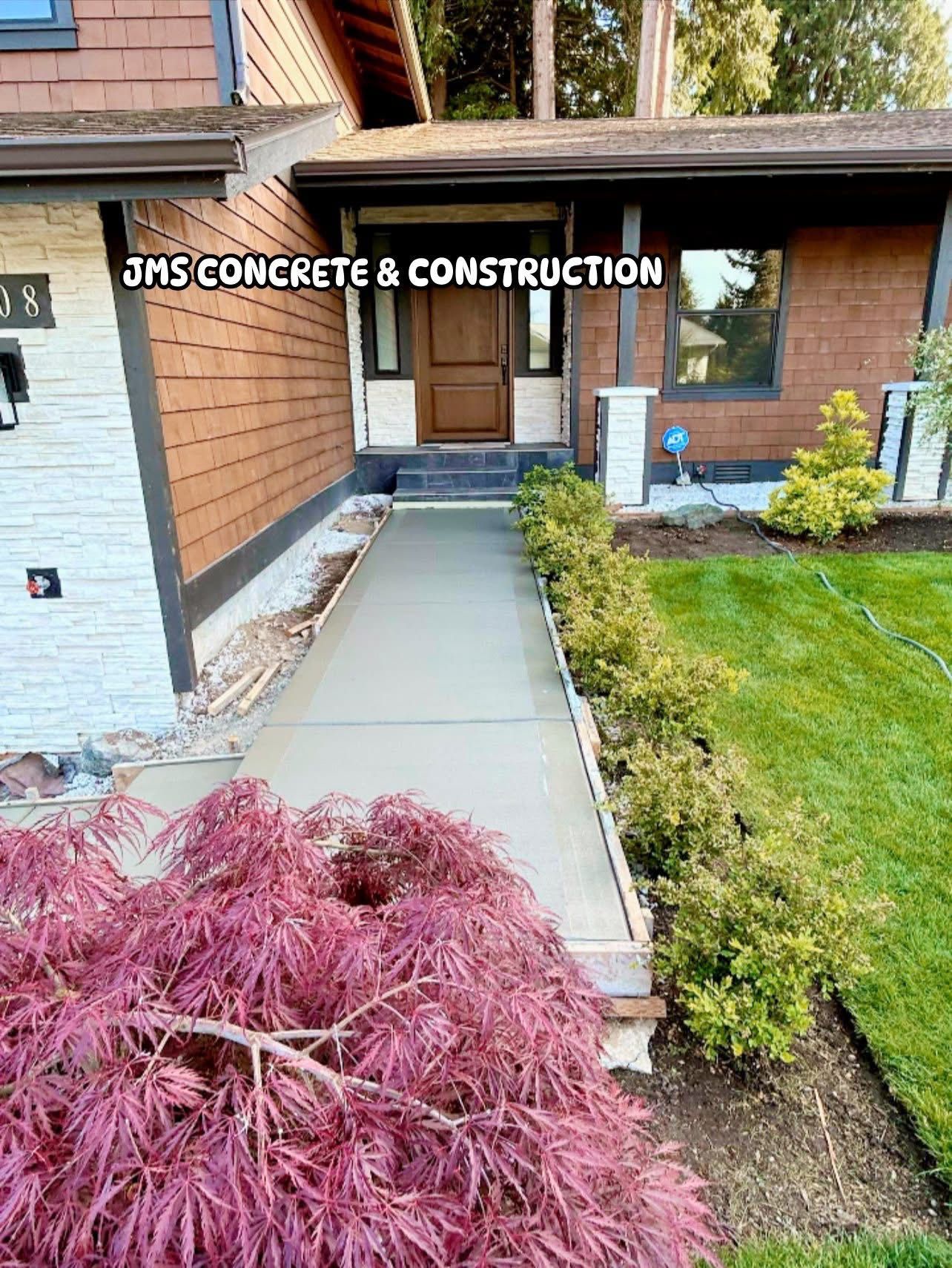 Newly poured concrete walkway leading to a house entrance; JMS Concrete & Construction sign visible.