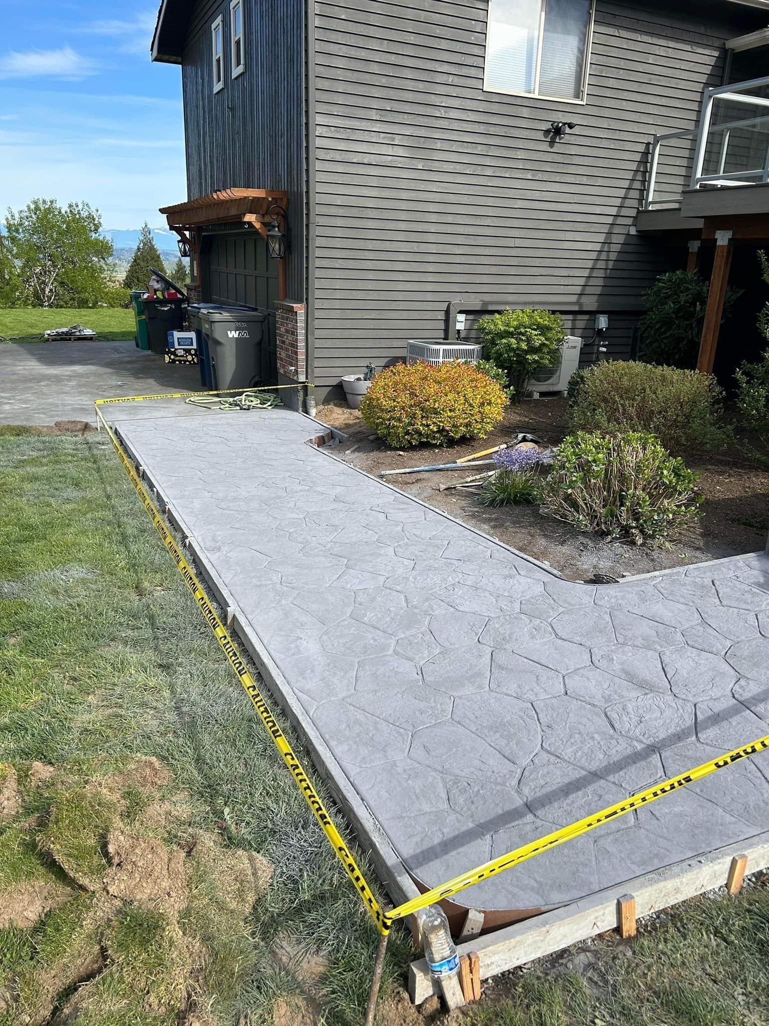 Newly poured concrete walkway next to a house, edged with wooden forms and caution tape.