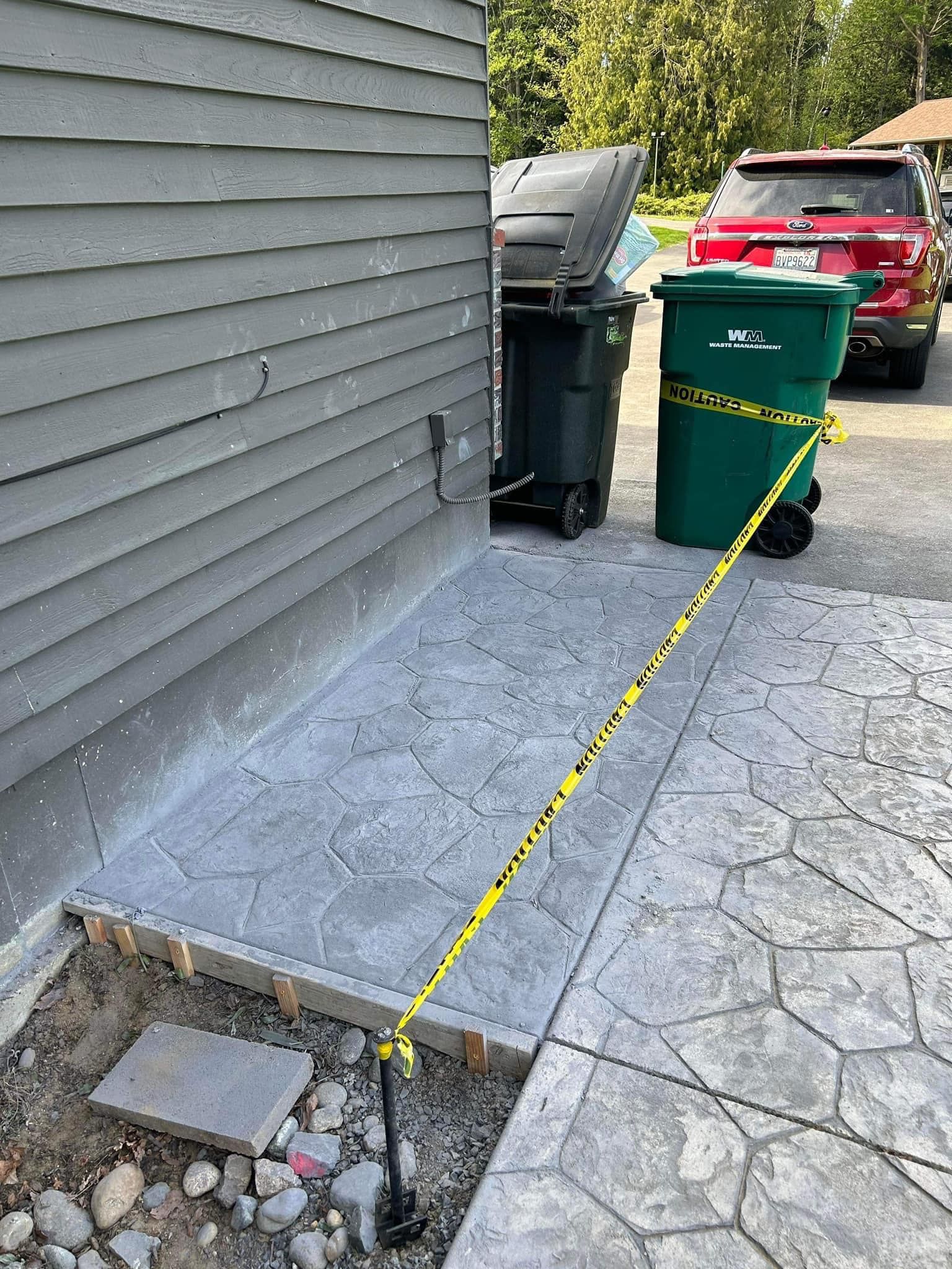 Stamped concrete area with trash cans, roped off with yellow caution tape, next to a gray building.