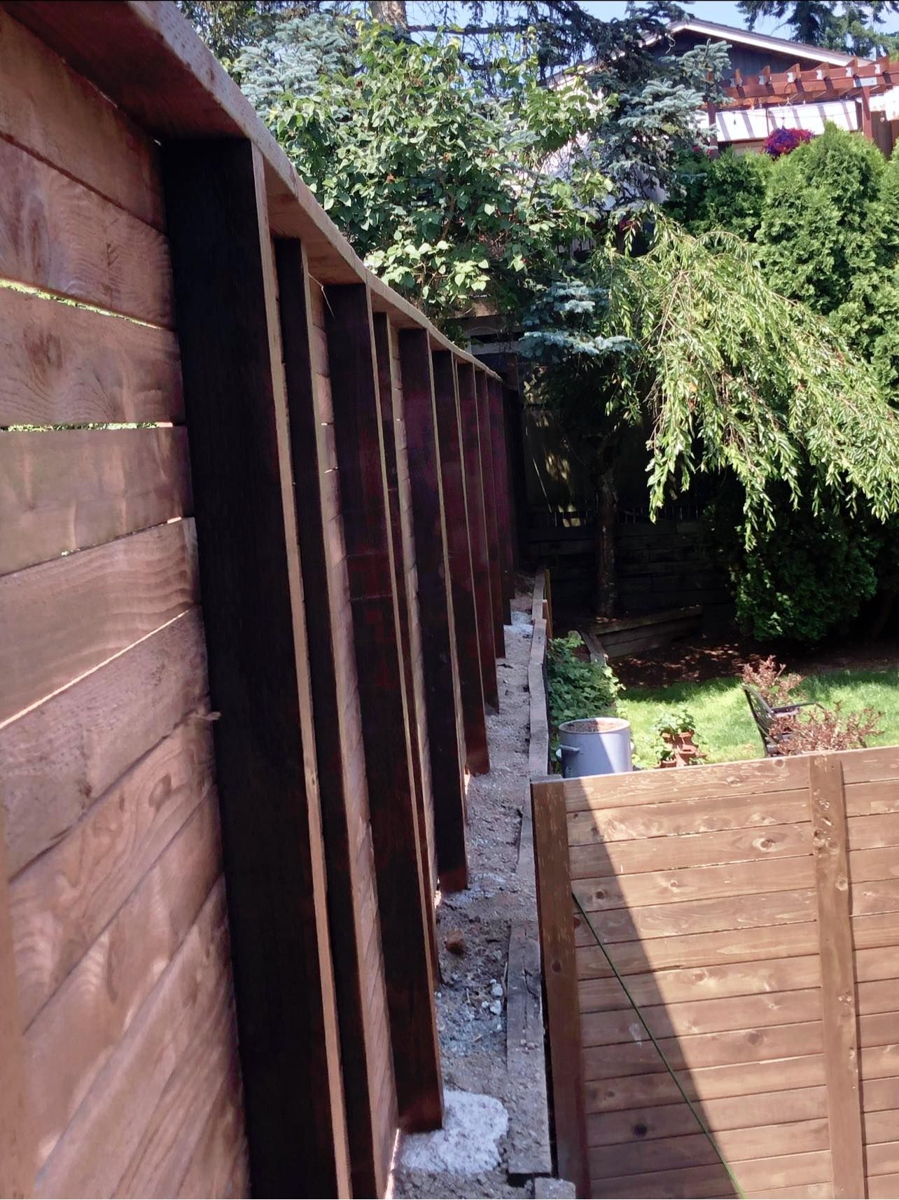 Wooden fence with vertical supports, surrounded by greenery.