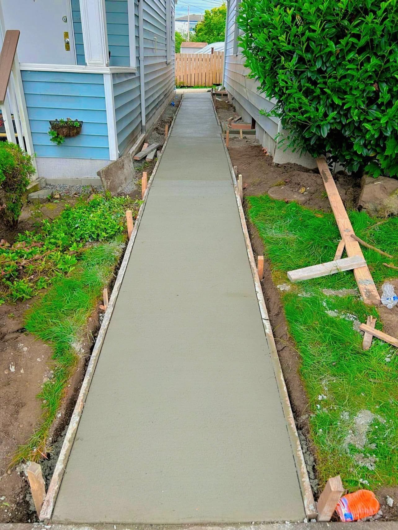 Freshly poured concrete walkway between two houses, wooden forms visible.