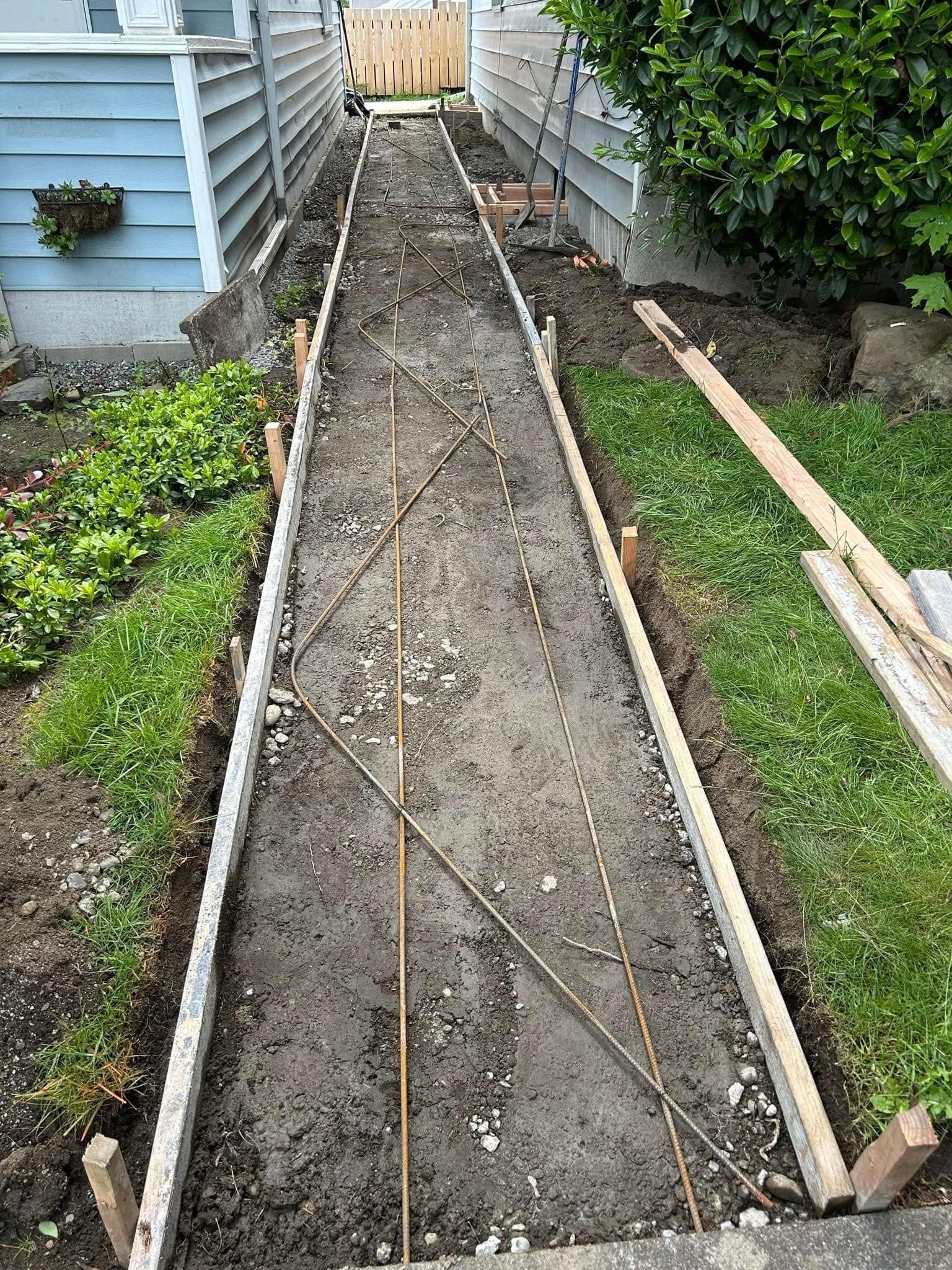 Pathway construction: Wooden forms define a narrow walkway with rebar laid. Earth is exposed.