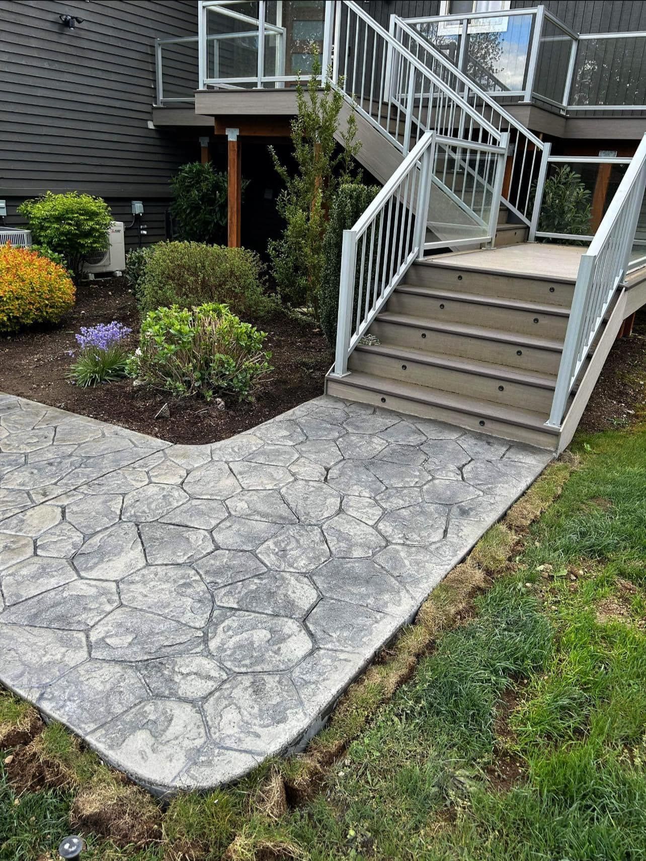 Stone pathway leading to stairs and a deck, surrounded by landscaping and grass.