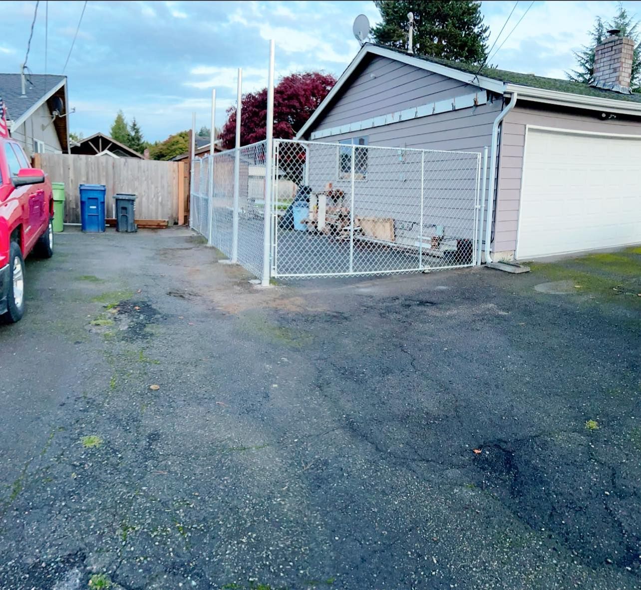 Backyard with chain-link fence, detached garage, trash cans, and red pickup truck. Asphalt surface.