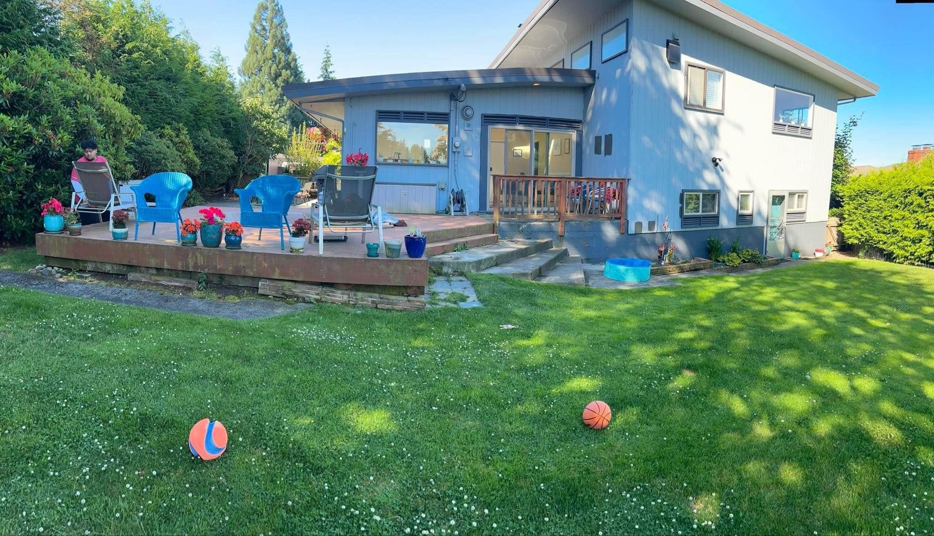 Backyard with house and deck. Lawn with balls. Blue chairs on deck.