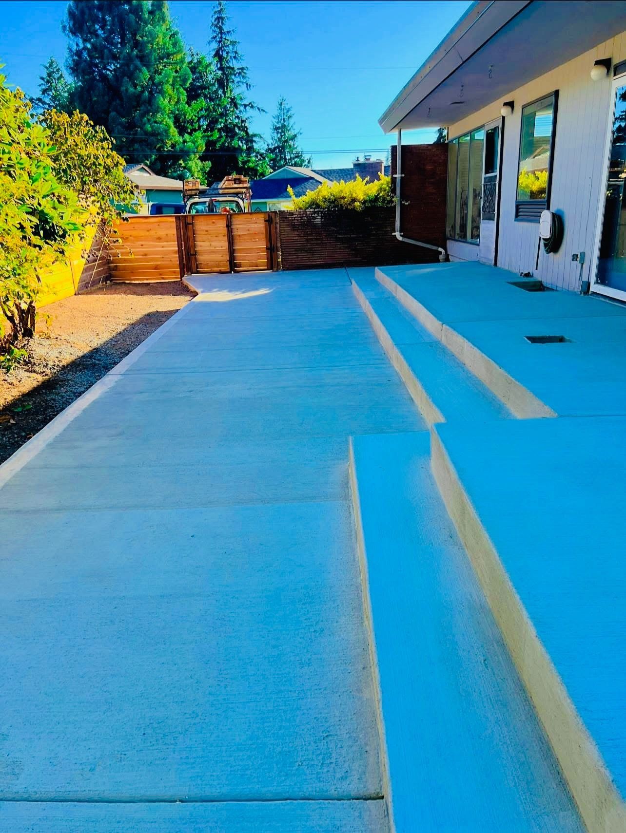 Concrete patio with steps leading to a modern house. Wooden fence in the background.