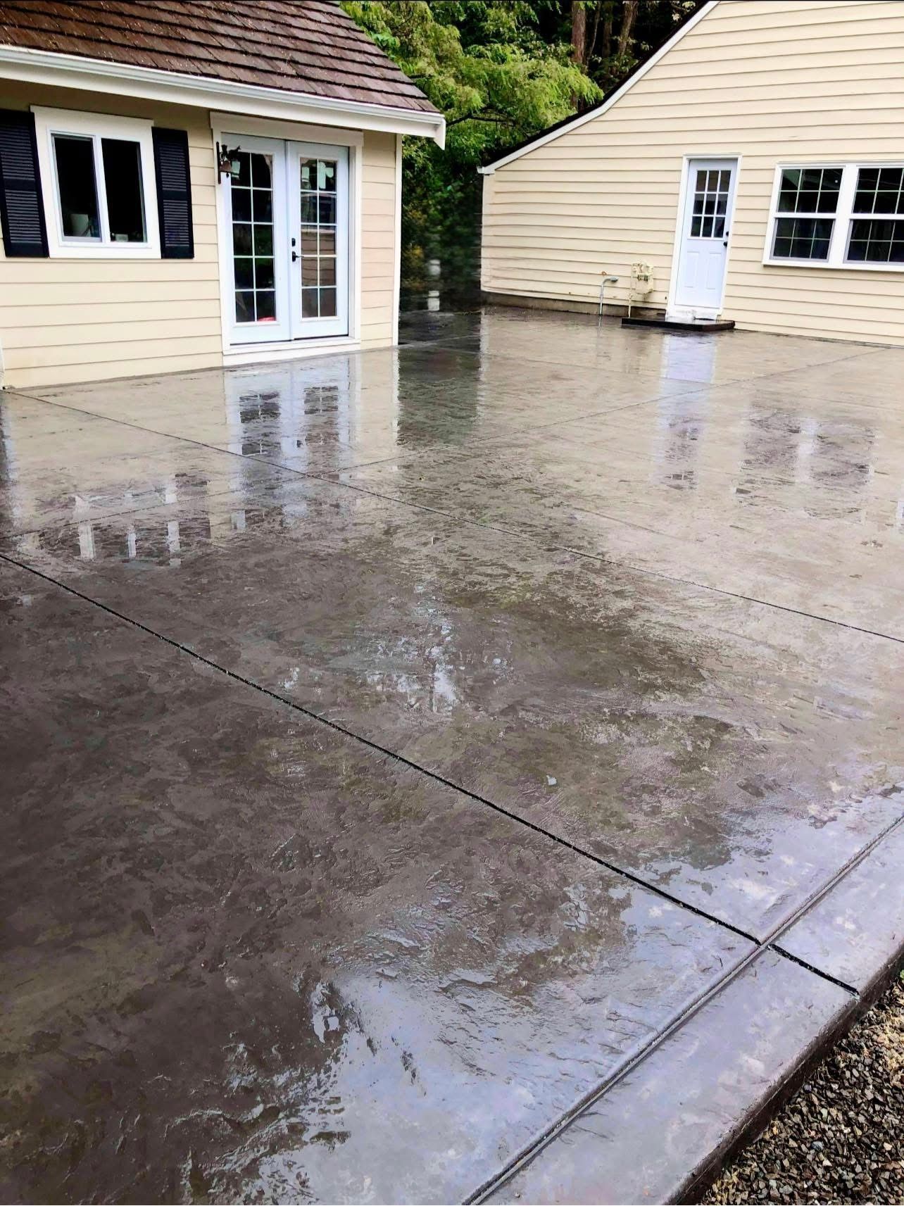 Wet concrete patio with two yellow-sided buildings and door reflections.