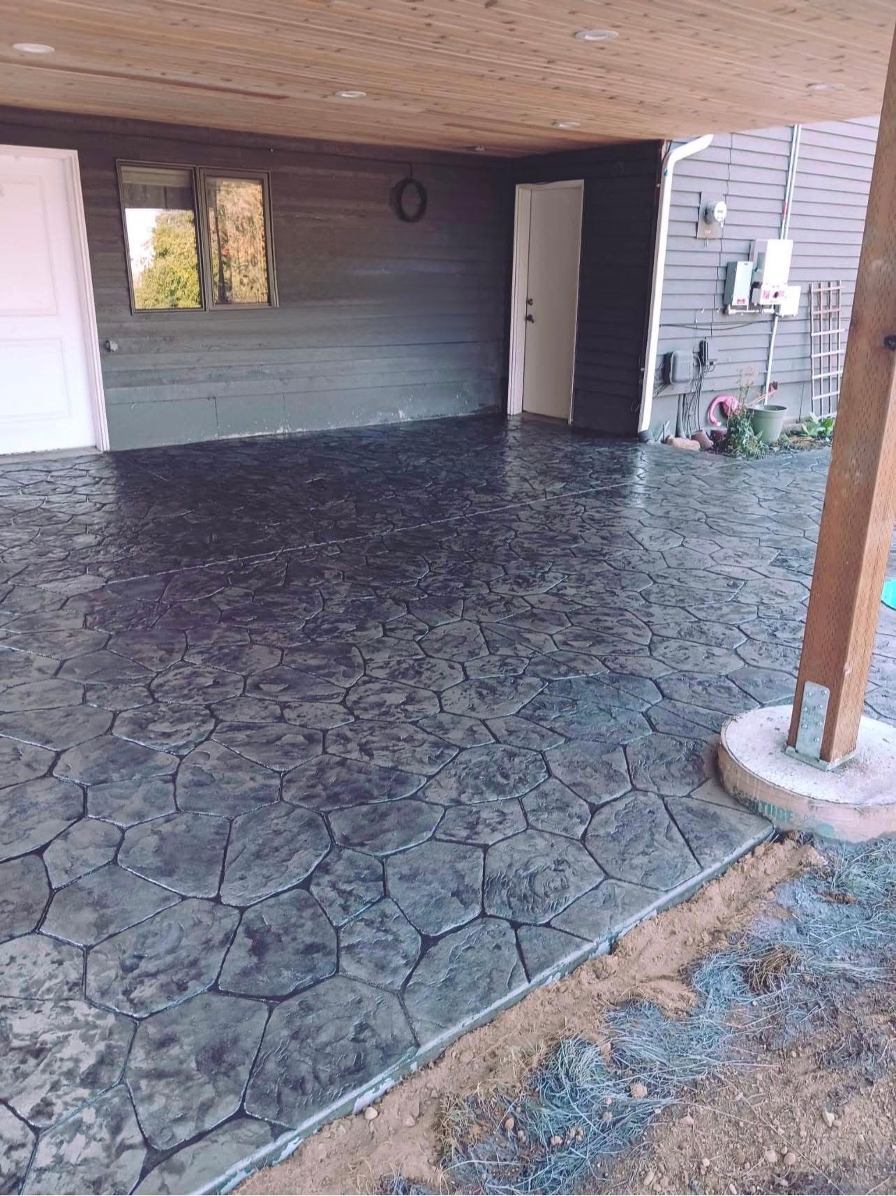Stamped concrete patio with a stone pattern, gray color, under a wooden deck.