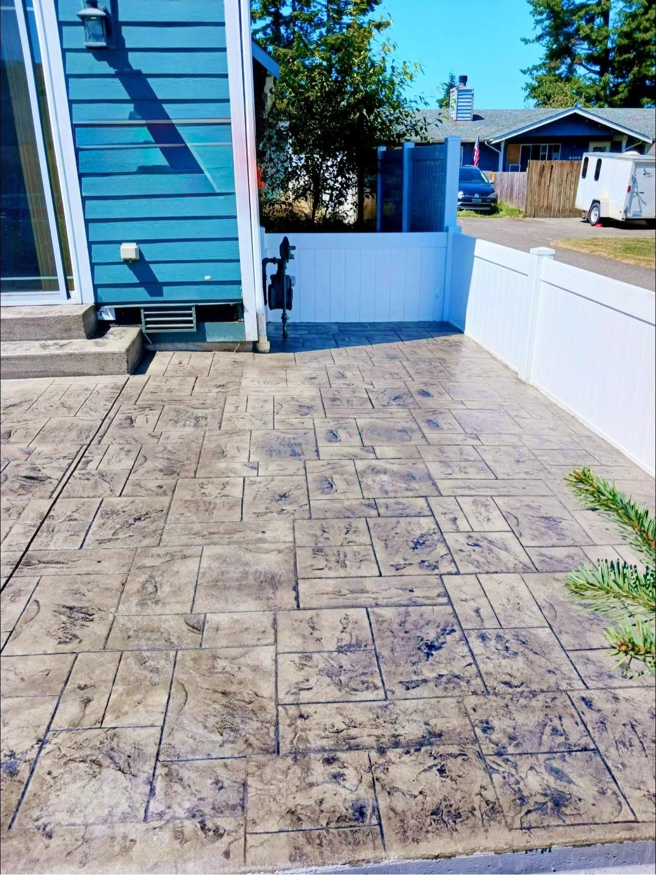 Stamped concrete patio next to a blue building with a white fence.