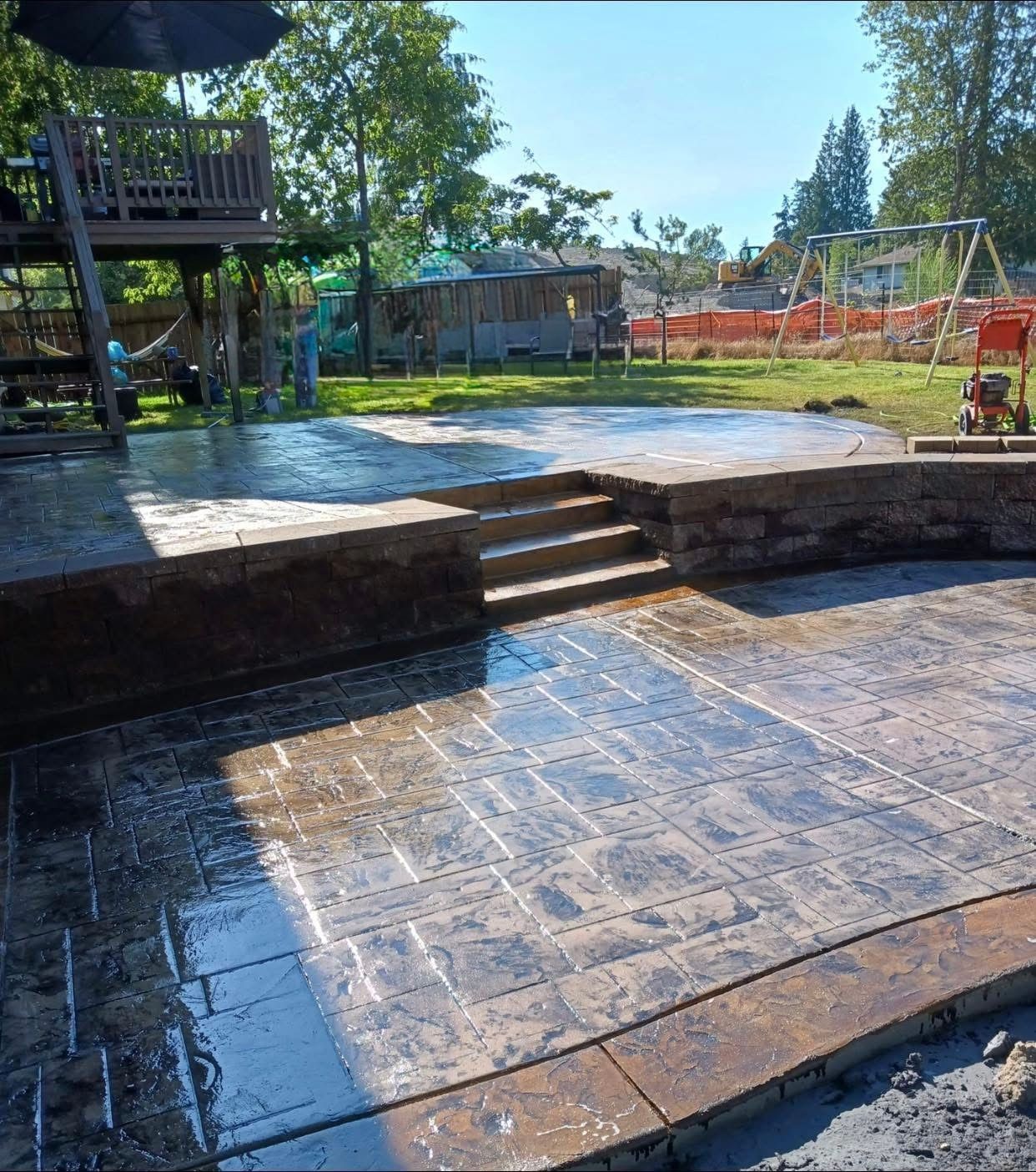 Stamped concrete patio with steps and retaining wall in a backyard setting.