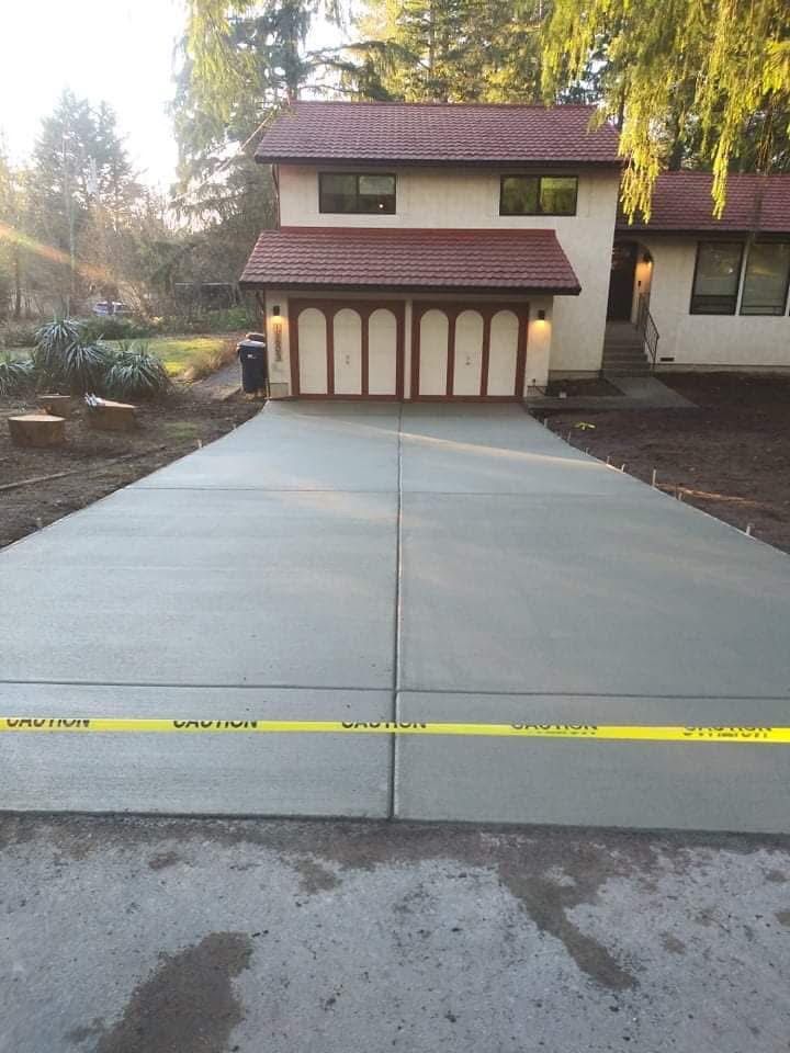Freshly poured gray concrete driveway in front of a house, with yellow caution tape.
