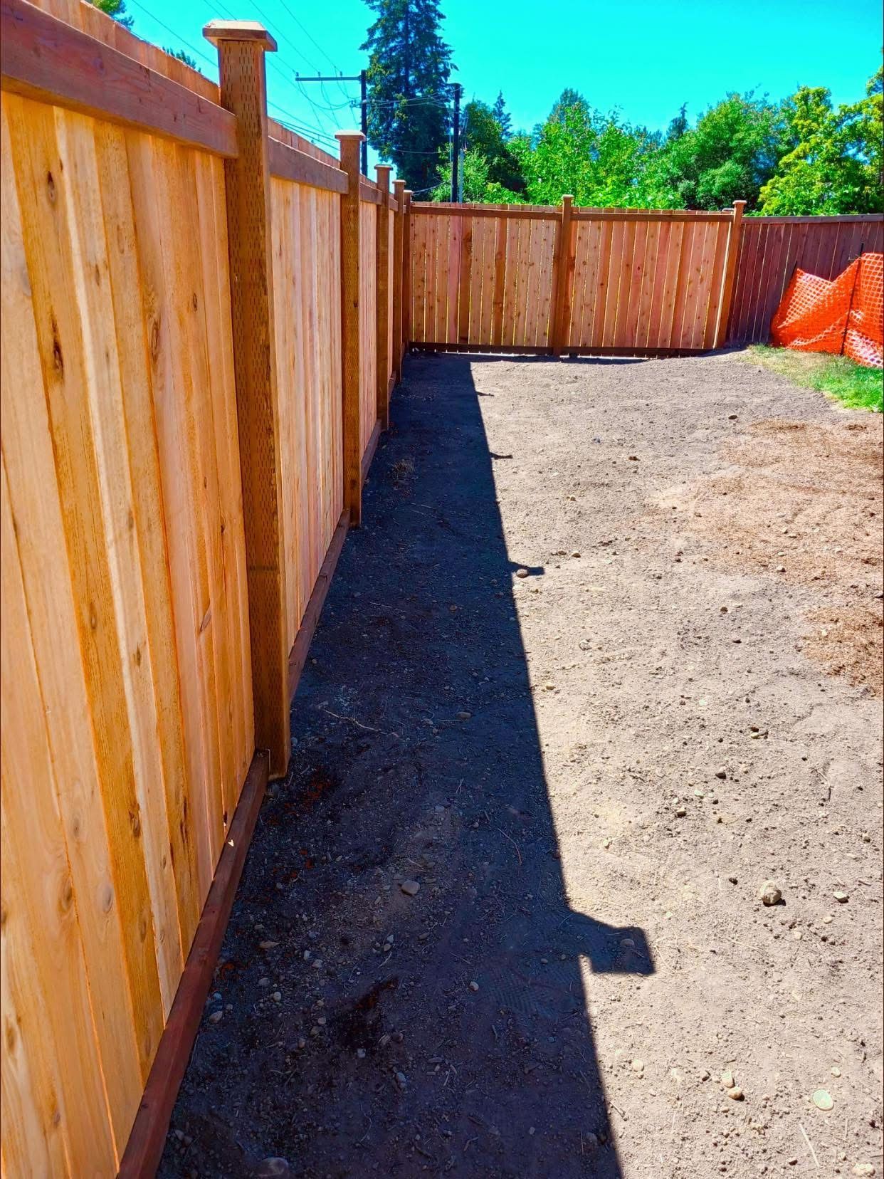 Wooden fence surrounds a dirt yard. A long, dark strip of fresh dirt runs along the fence.