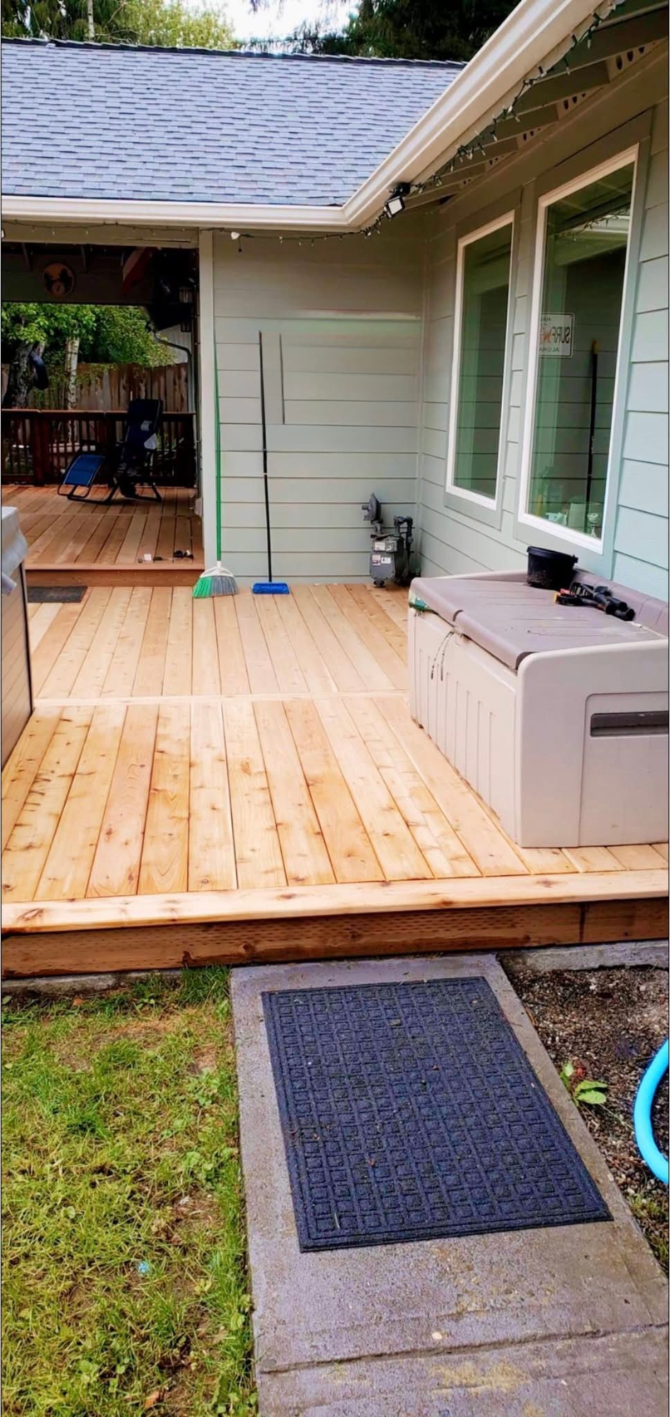 Backyard deck with a spa, next to a building with windows. A doormat is on the ground.