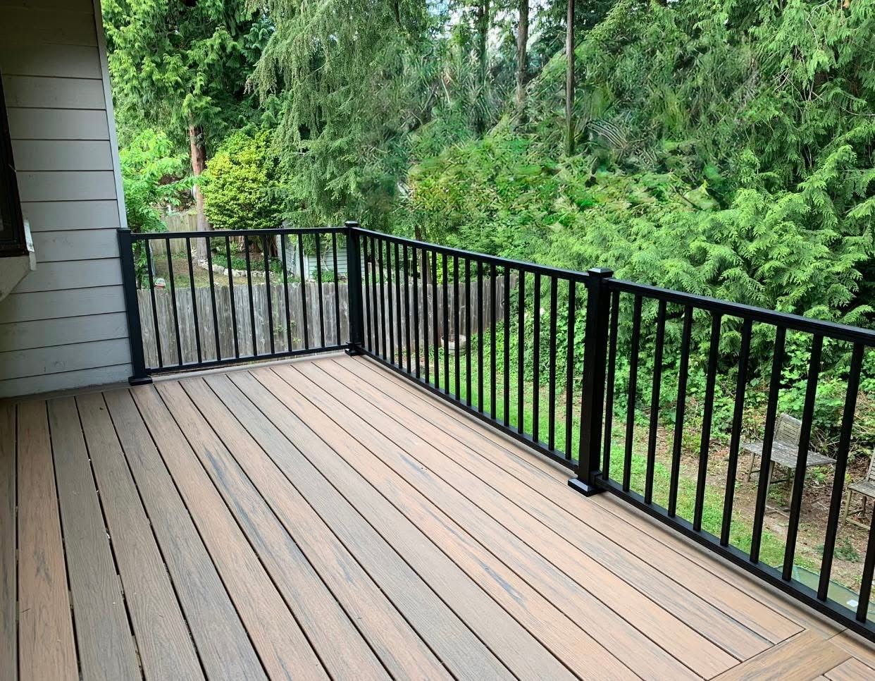 Deck with black railing, brown composite decking, and a backdrop of green trees.