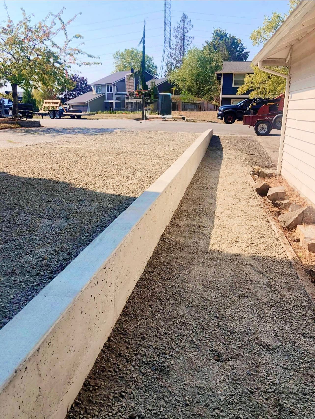 Concrete retaining wall along gravel parking area next to a building.