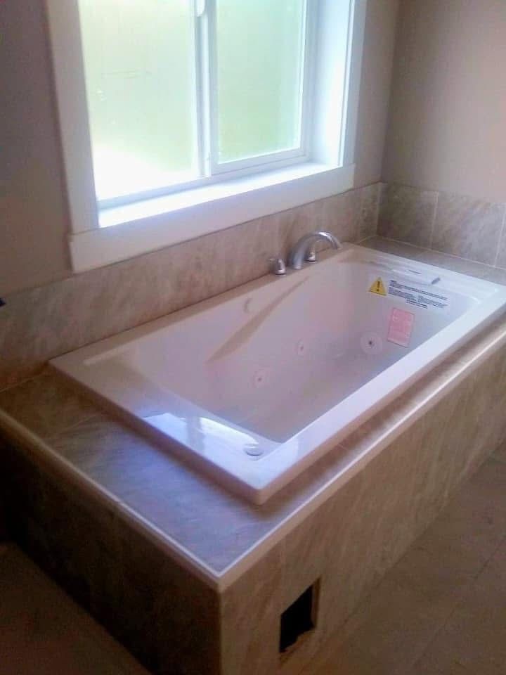 Built-in bathtub with beige tile surround, near a window. A faucet is visible.