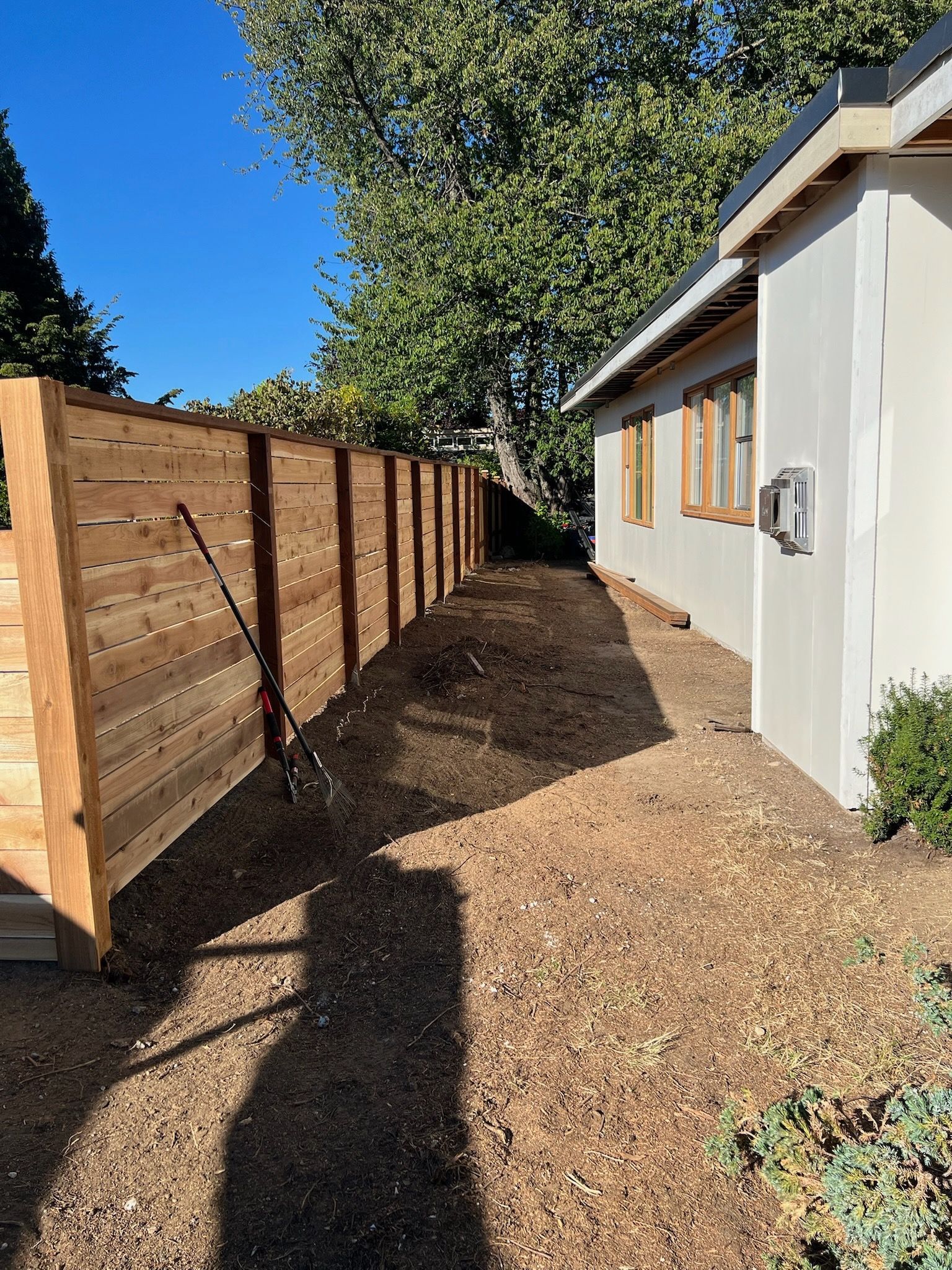 A wooden fence and light-colored building sit side by side on a sunny day.