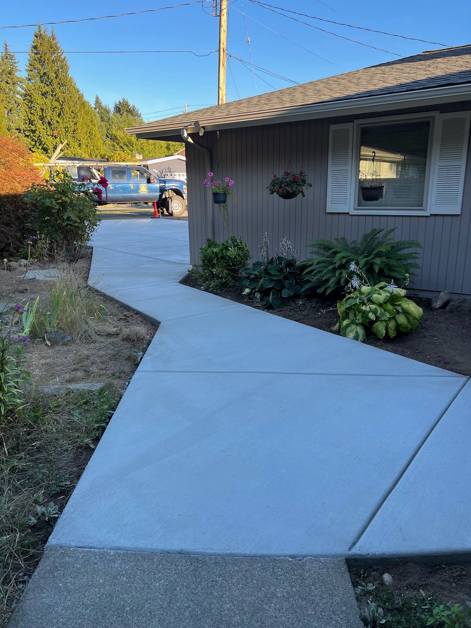 Newly poured concrete walkway leading to a house with shutters and hanging flower baskets.