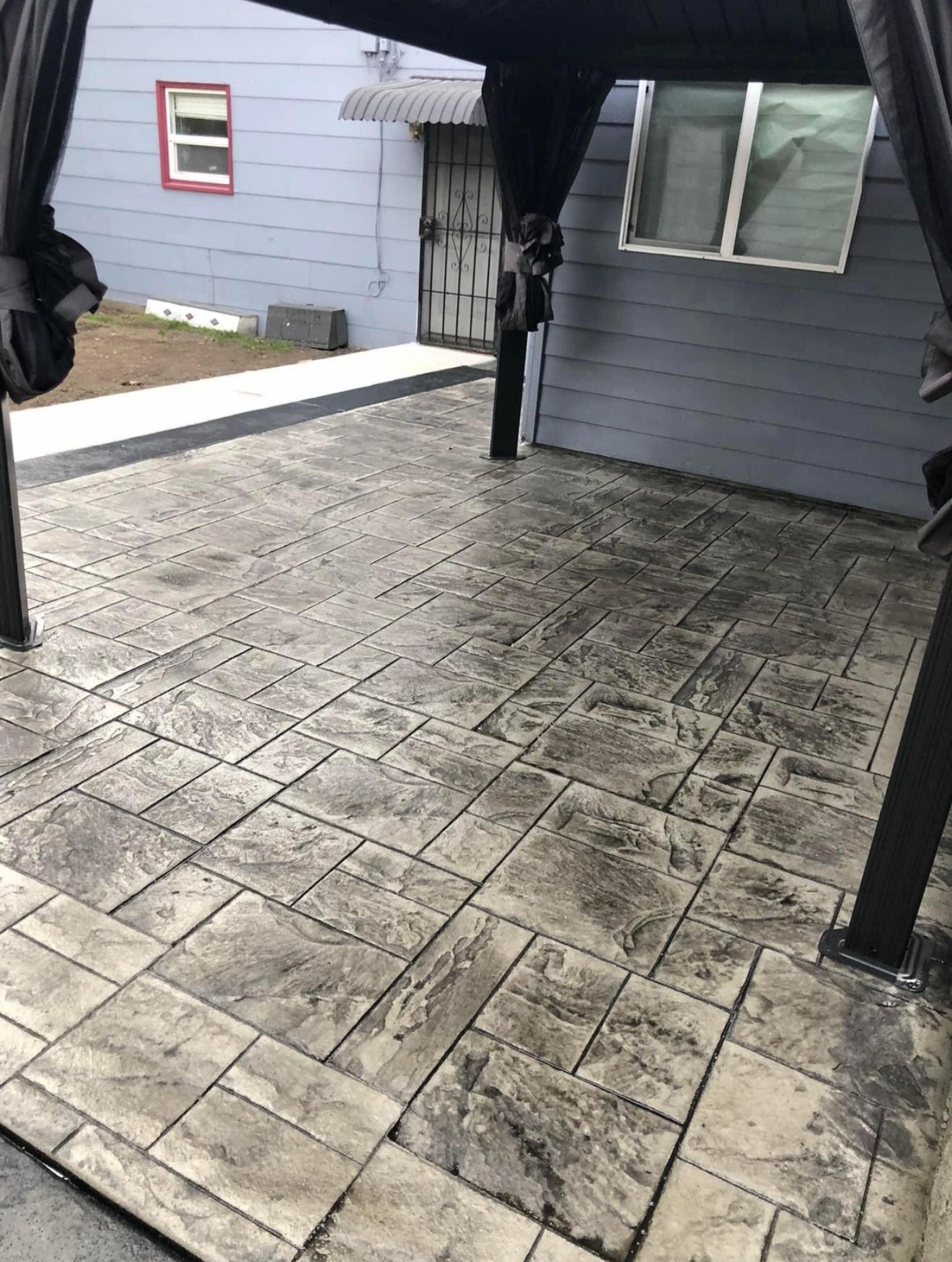 Patio with gray stamped concrete, covered by a black canopy. Buildings in the background.