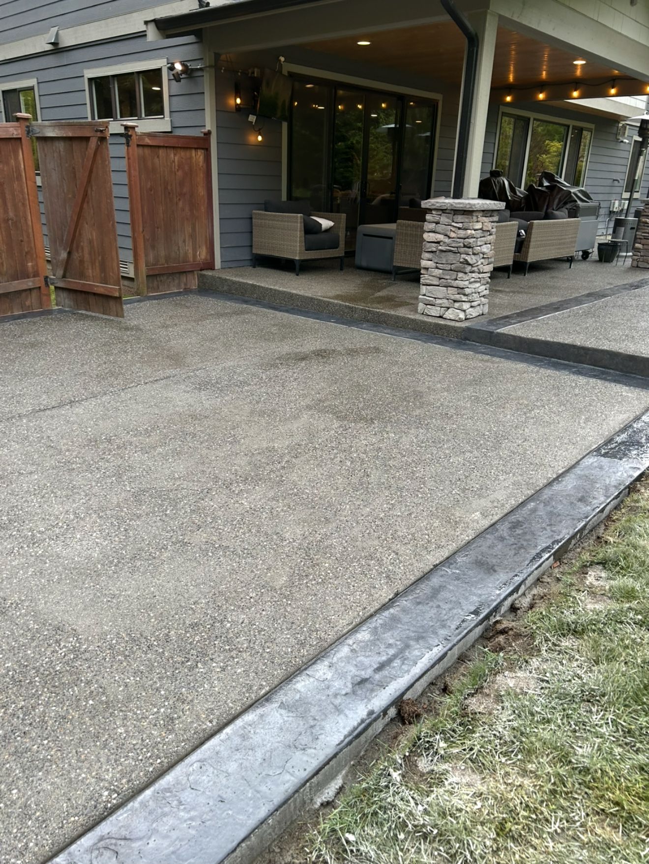 Concrete patio with black border, adjacent to grass, under a covered outdoor seating area.