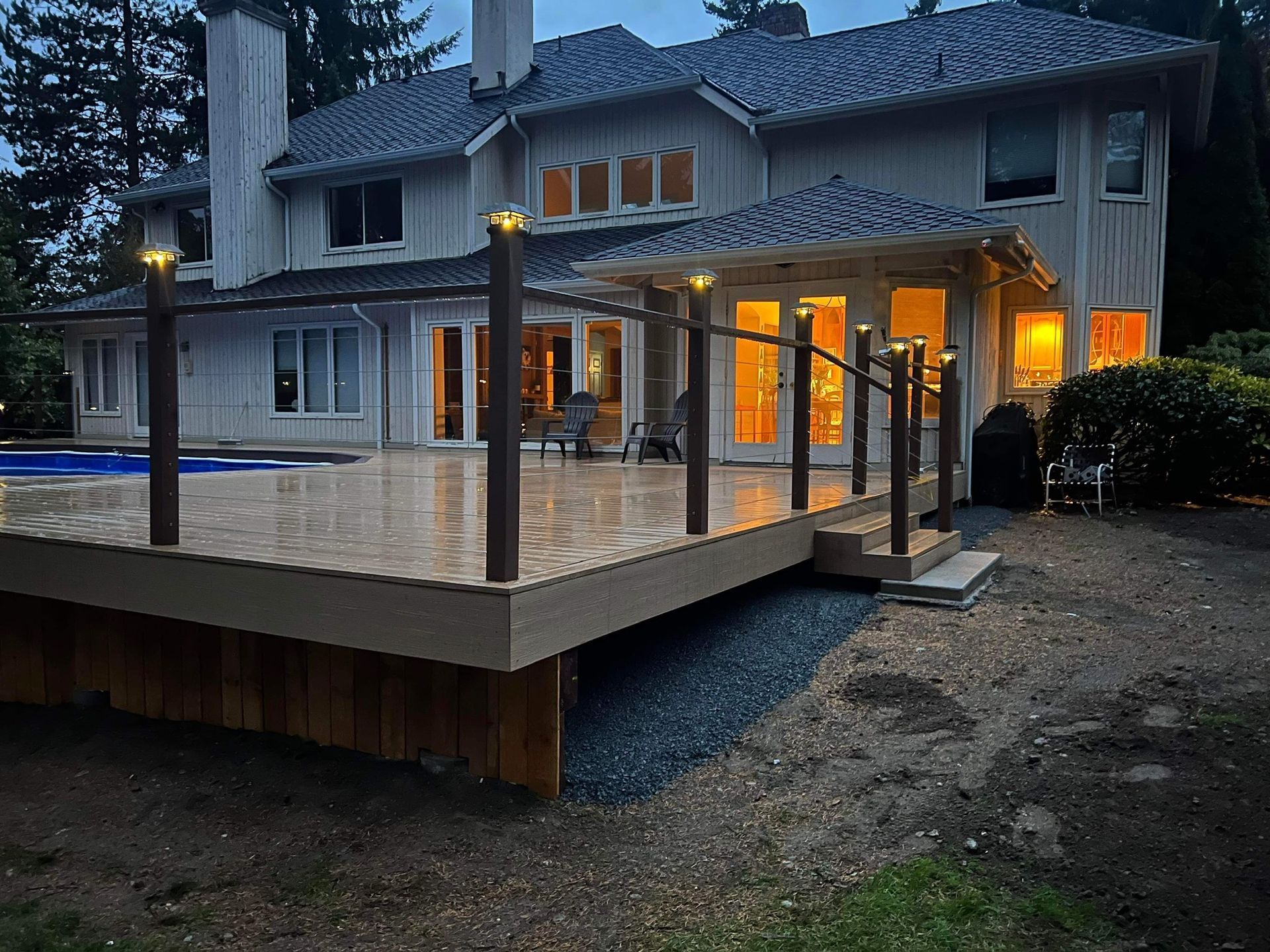 Two-story home with a large deck and pool. Deck has railing with lights, overlooking a backyard and pool.