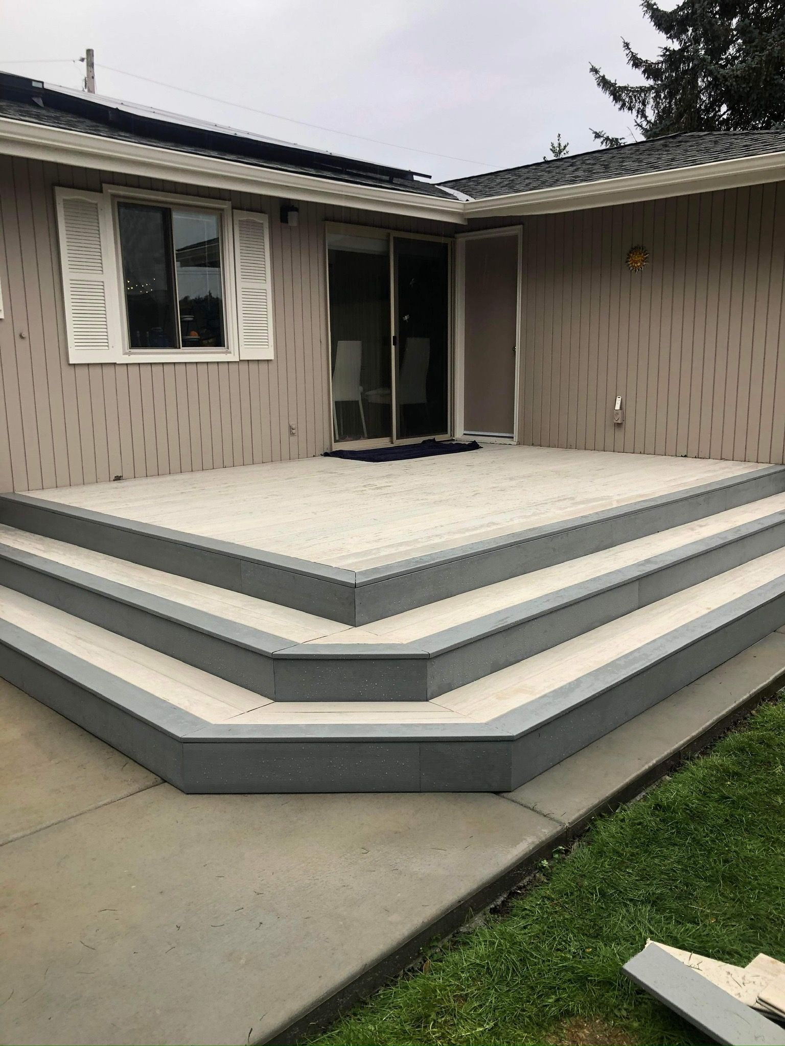 Grey composite deck with three steps leading to sliding glass doors and a window.
