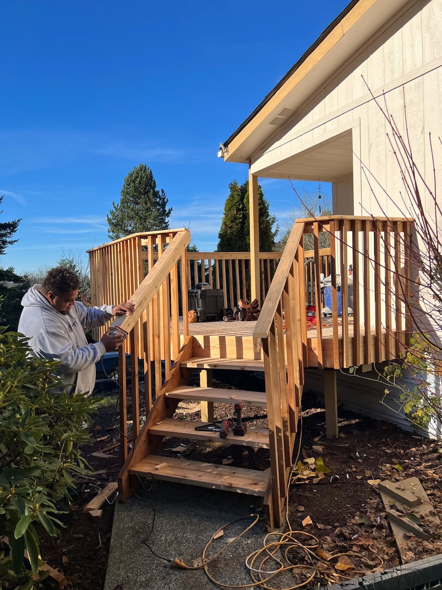 Man constructing a wooden deck with stairs next to a house on a sunny day.