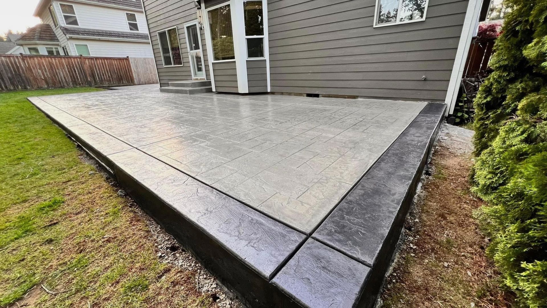 Concrete patio with dark border, adjacent to a house with gray siding.