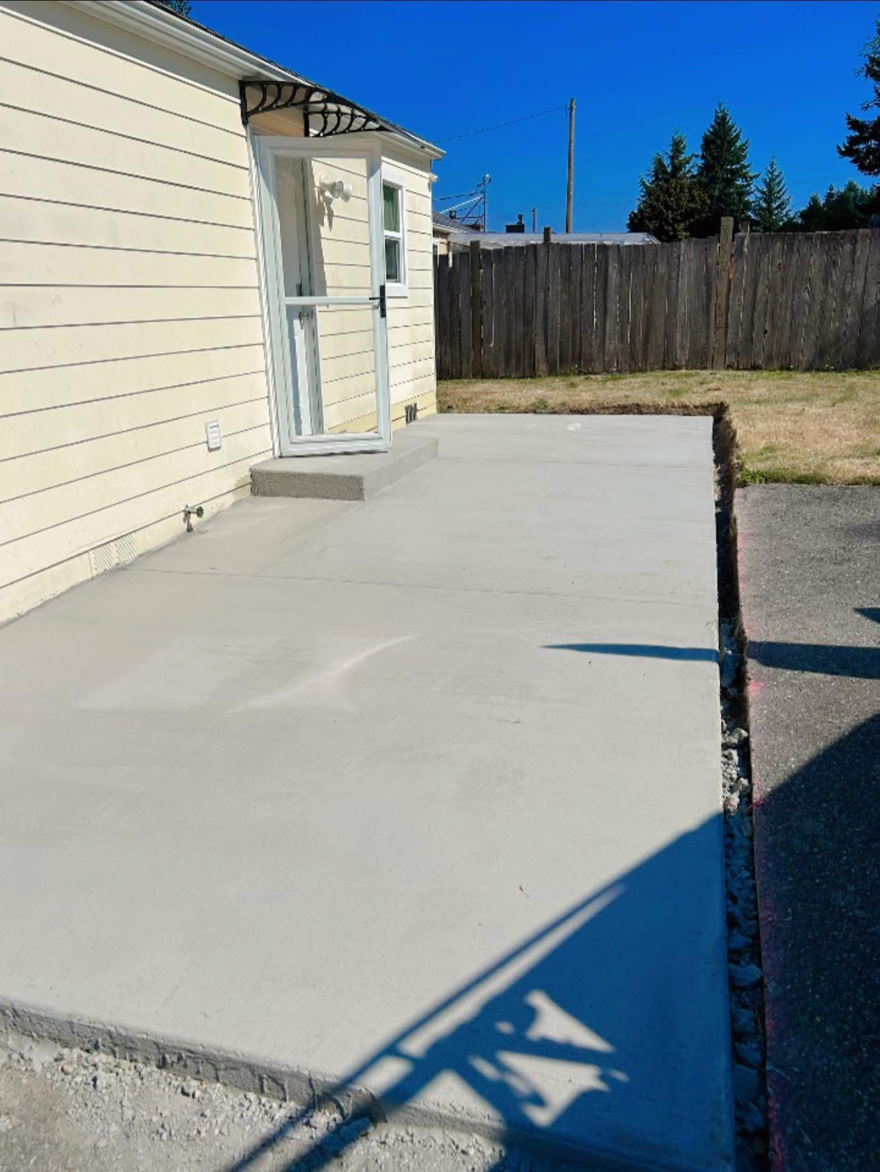 Freshly poured concrete patio next to a light yellow house and fence, sunny day.