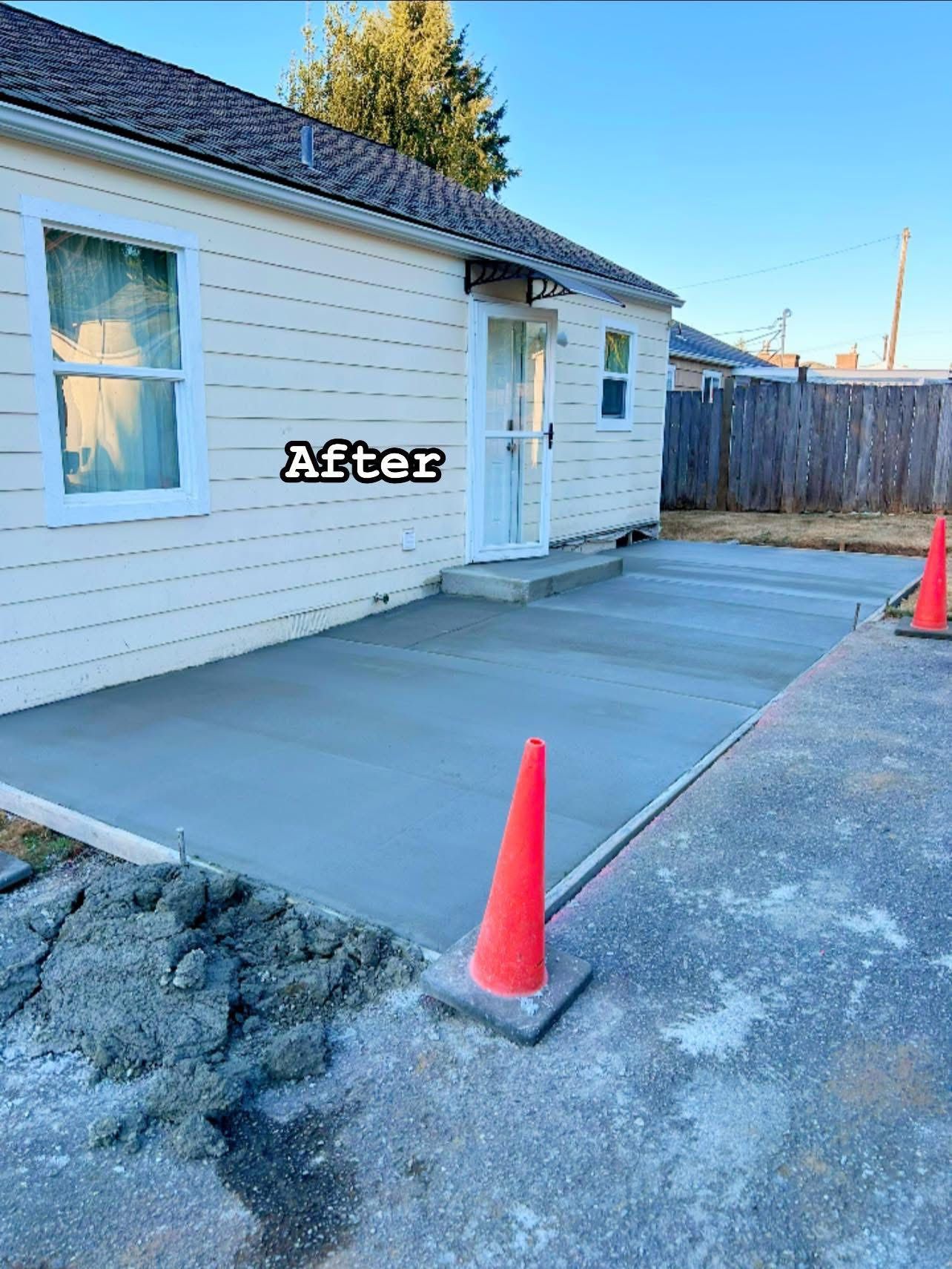 Newly poured concrete patio next to a cream-colored house. Orange traffic cone visible.